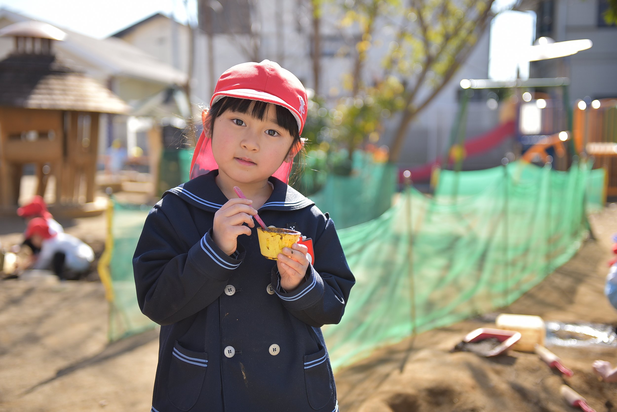 幼い女の子が公園の砂場でアイスクリームを食べている。