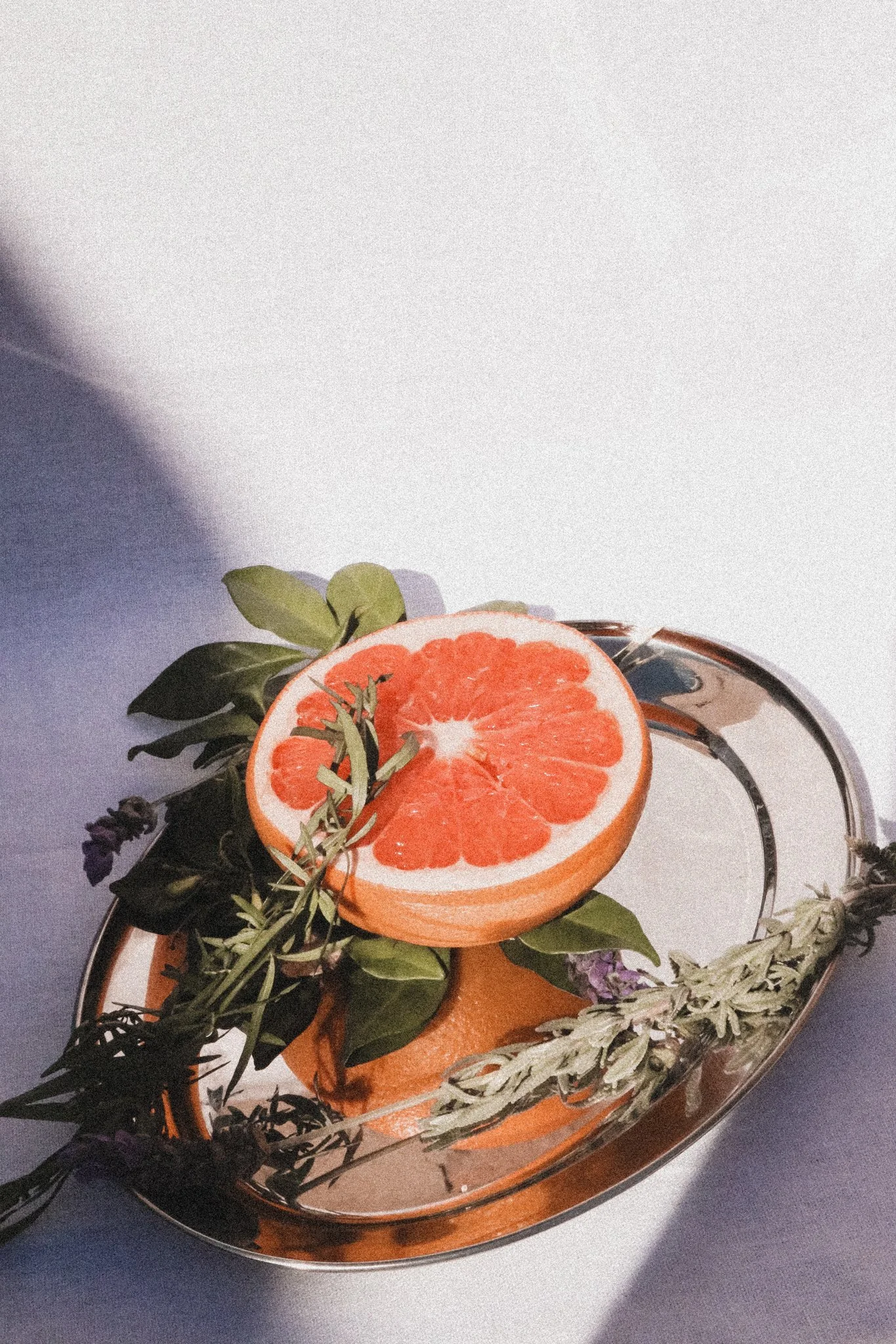 Half of a grapefruit on a silver tray with lavender and rosemary.