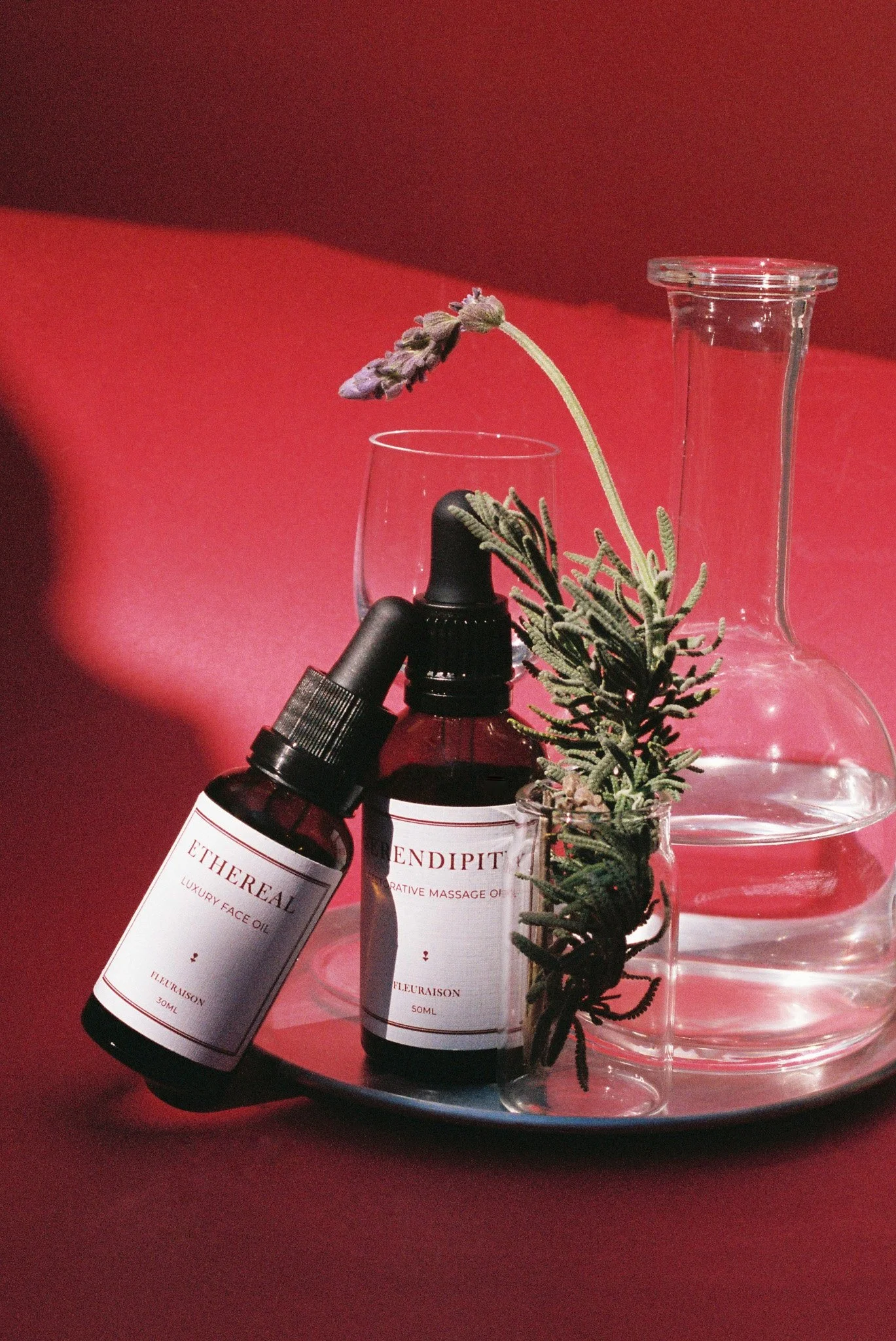 Fleuraison Ethereal Face Oil and Serendipity Massage Oil on a silver tray styled with rosemary and lavender.