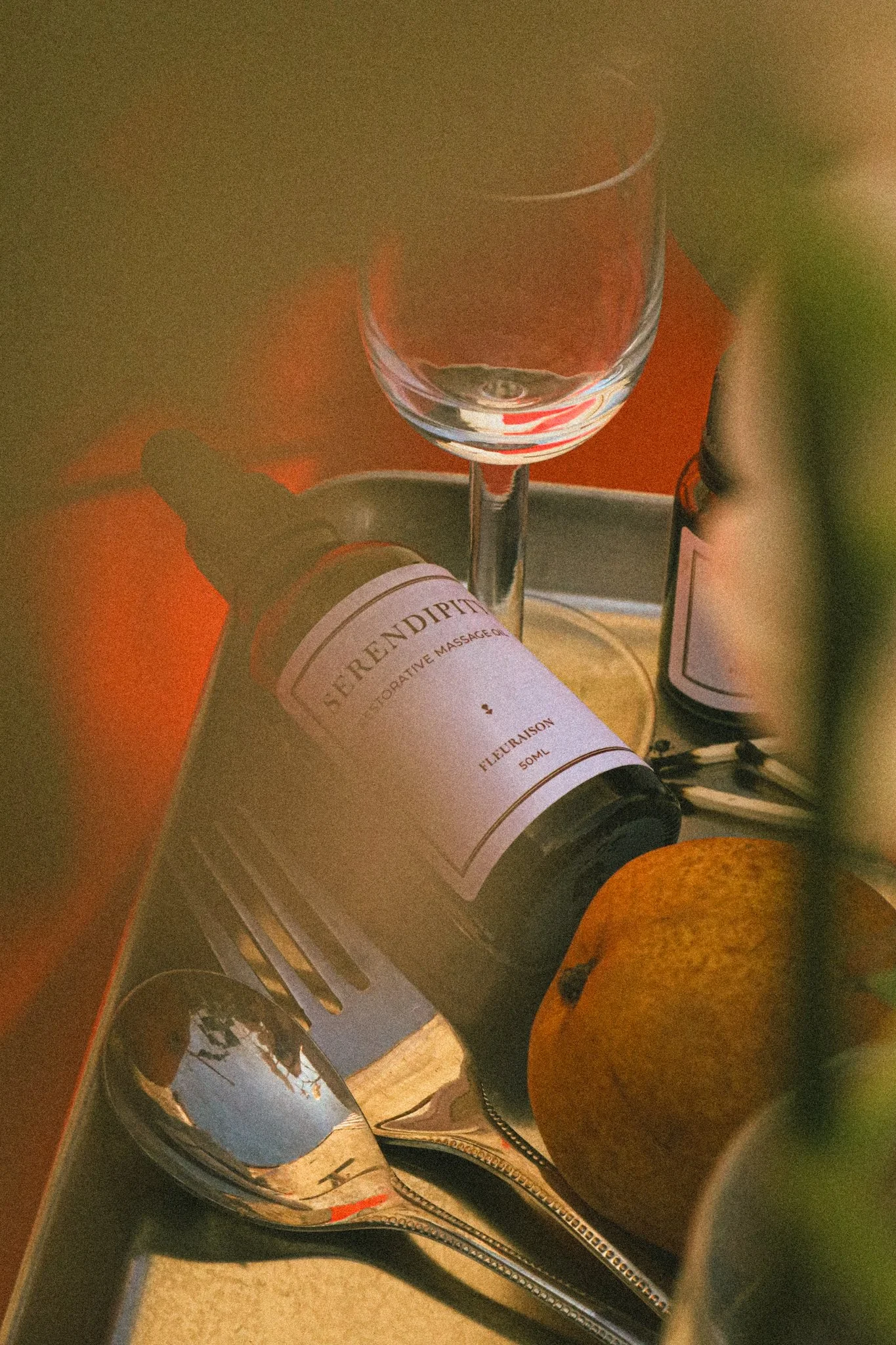 Fleuraison Serendipity Massage Oil displayed silver tray styled with a glass, lemon, cutlery and partially obscured by greenery.