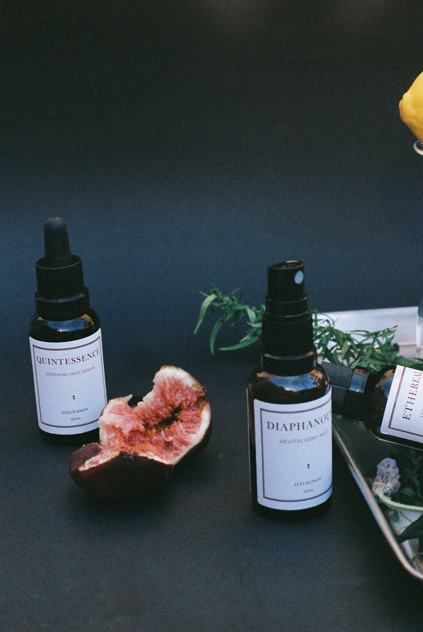 Fleuraison Quintessence Face Serum and Diaphanous Mist styled with a cut fig, green foliage and silver tray.