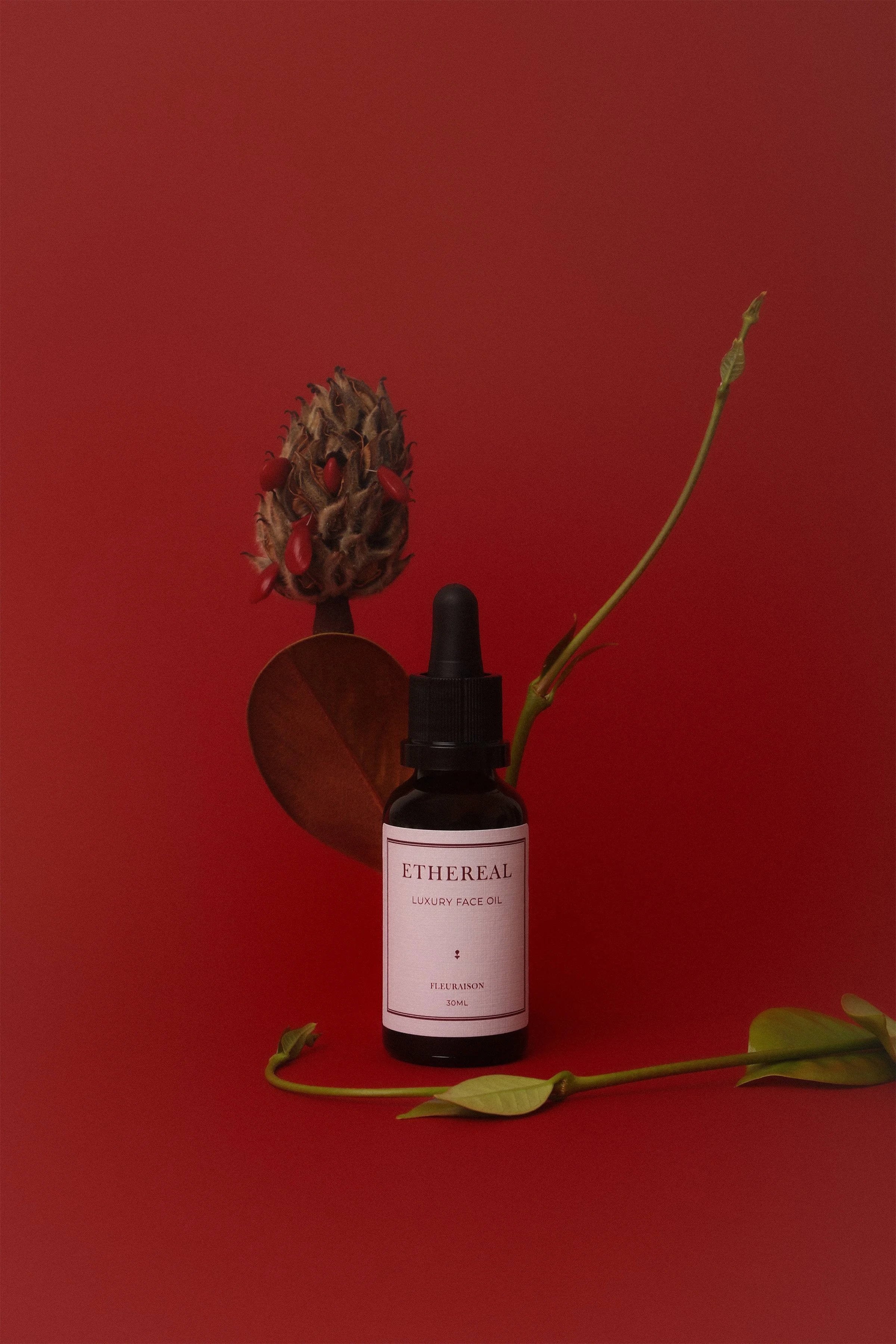 Luxury face oil styled with botanicals against dark red backdrop
