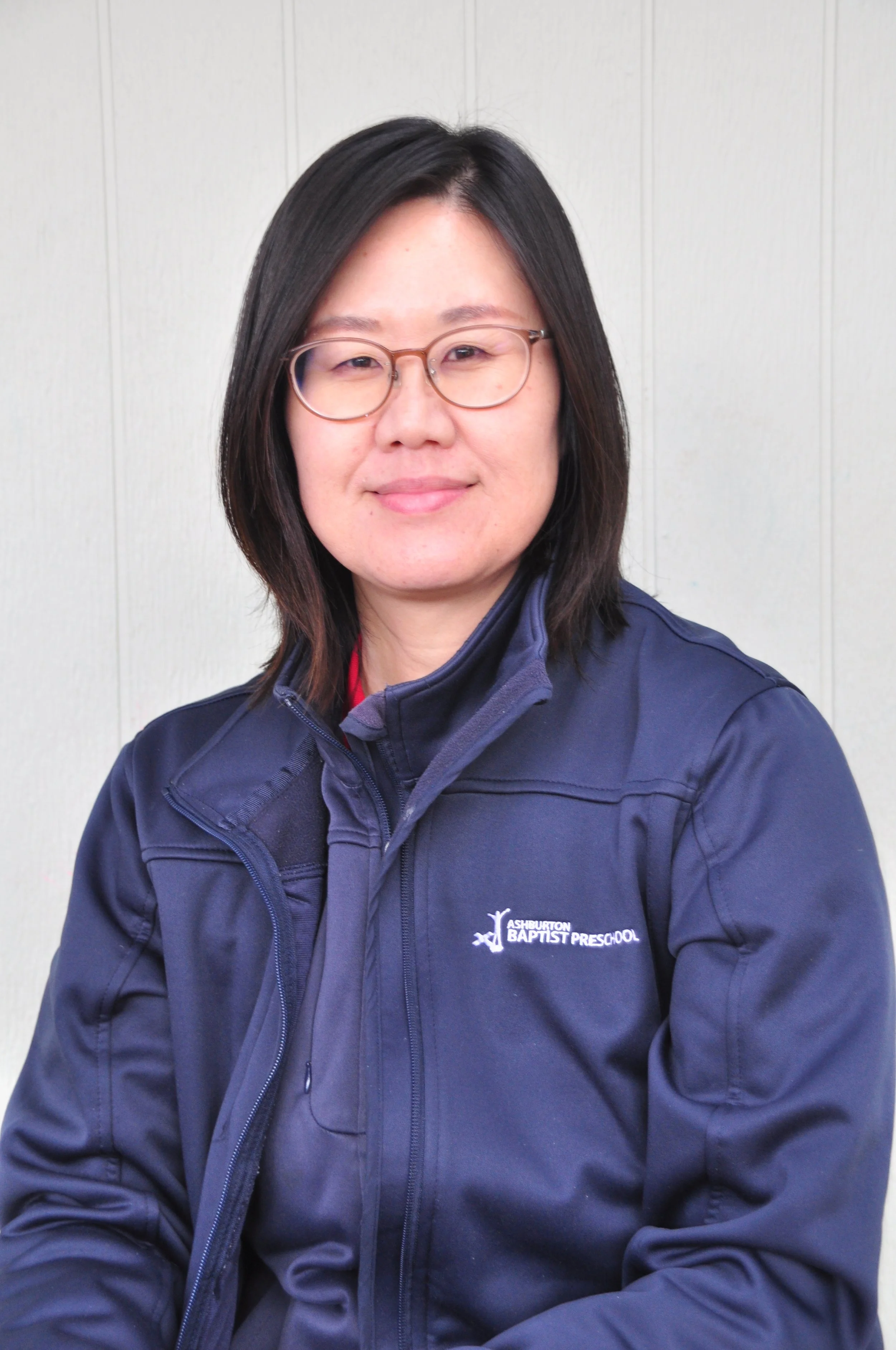A woman with glasses and shoulder-length hair, wearing a sporty vest, leaning on a railing outdoors with a slight smile.