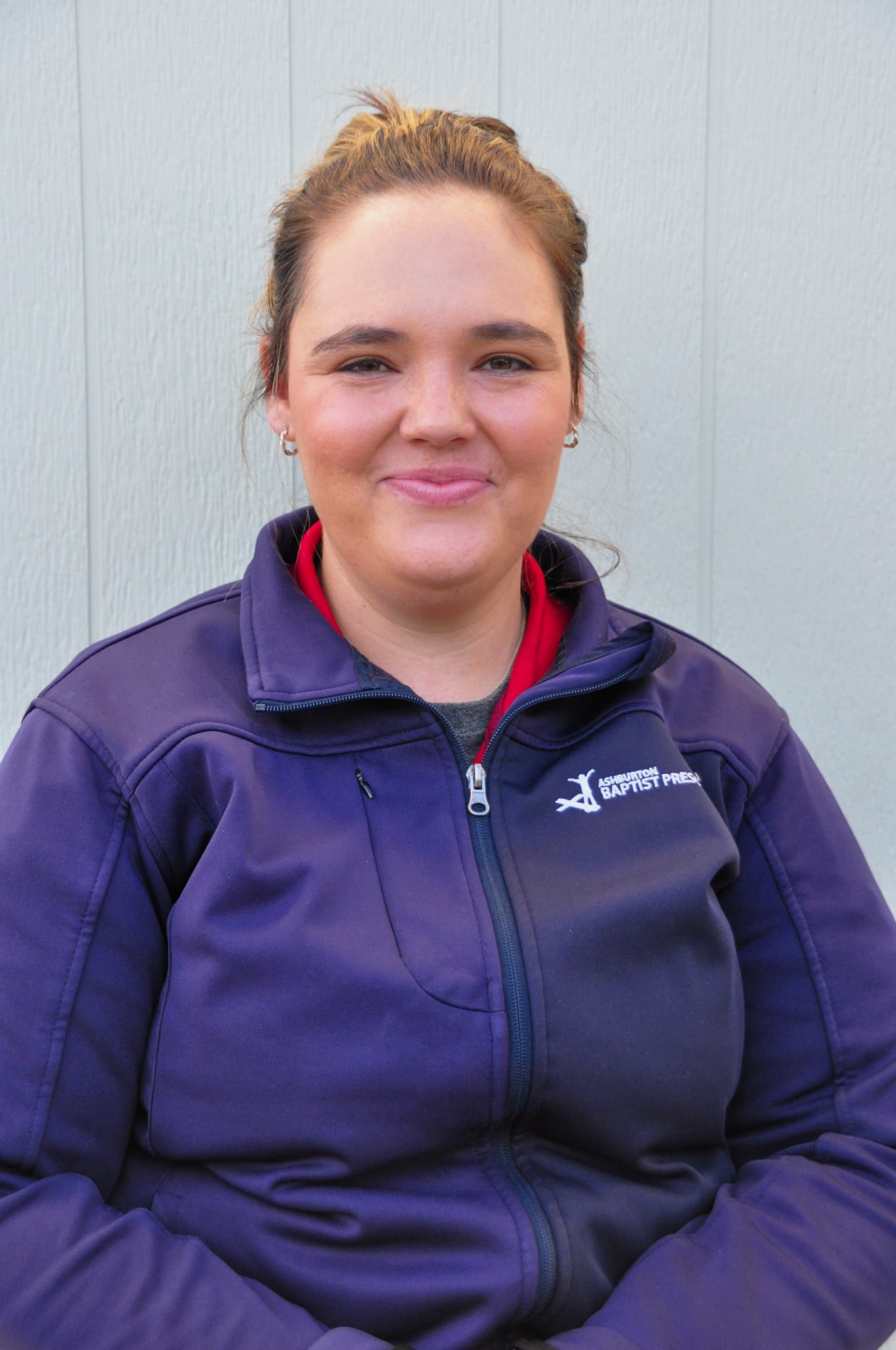 A smiling woman with glasses and a nose ring, wearing a red and navy jacket, standing outdoors with her arms resting on a black railing.