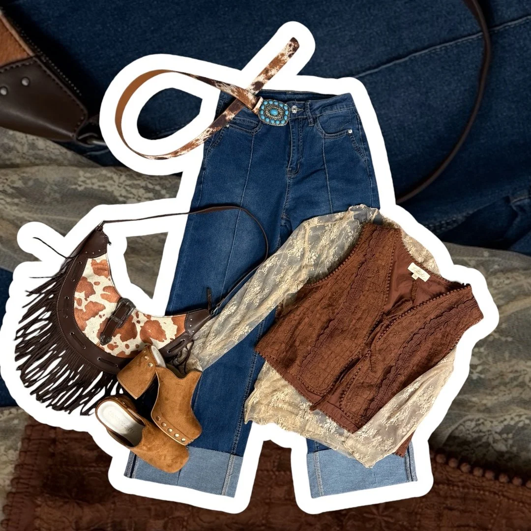 Folded clothes and accessories including a pair of blue jeans, a patterned handbag with fringe, a pair of brown ankle boots, a brown and cream lace blouse, and a brown vest.