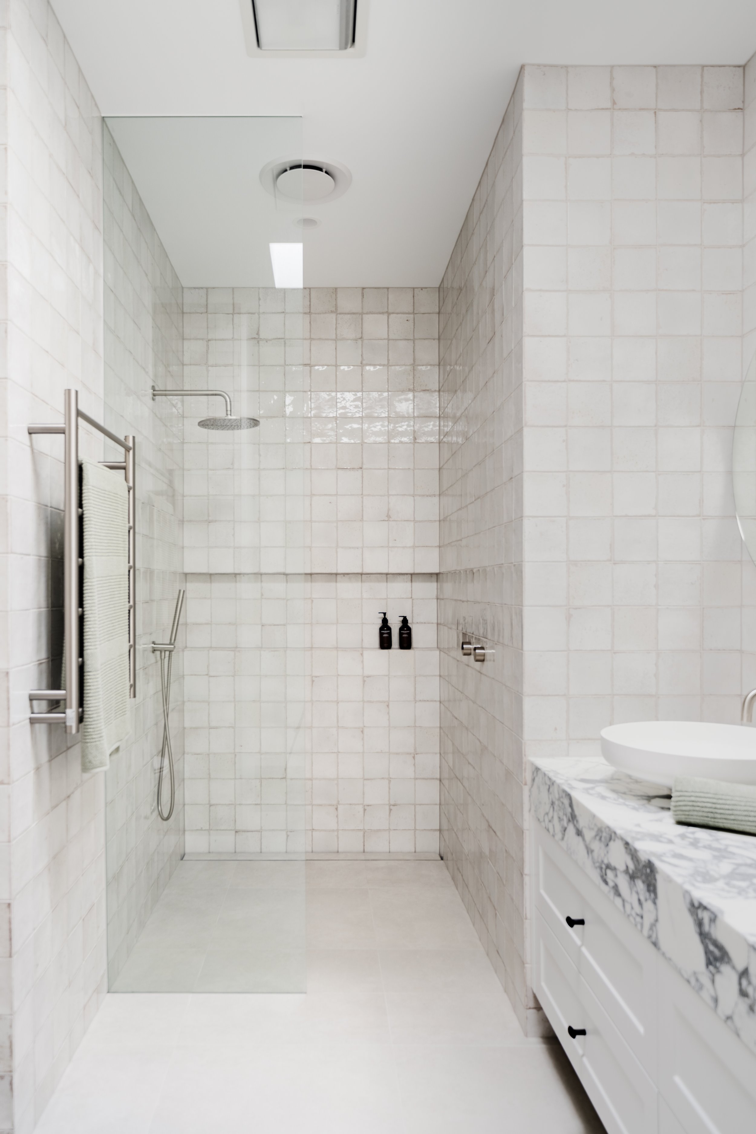 Modern bathroom with walk-in shower, glass partition, wall-mounted showerhead, and a white vanity with a vessel sink and marble countertop.