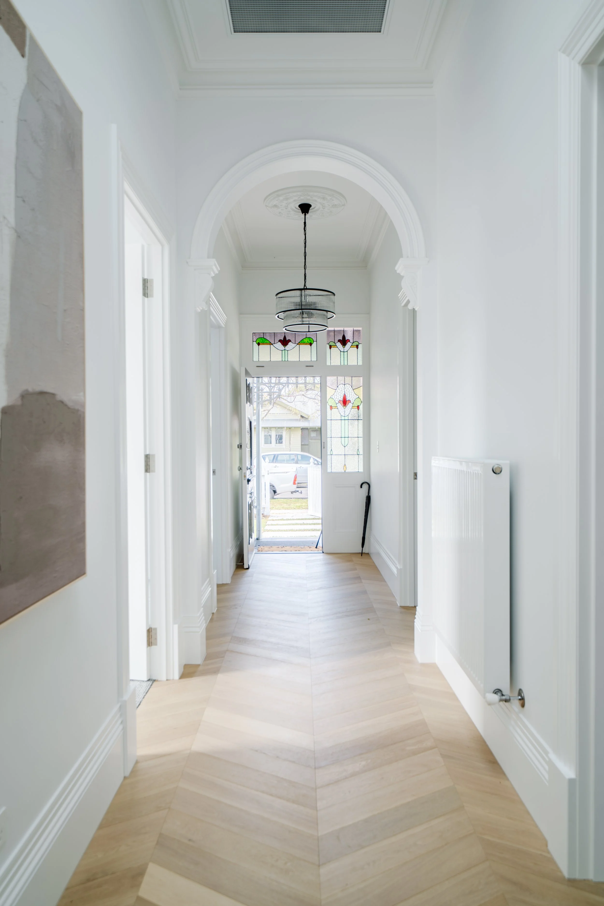 Bright entryway with white walls, detailed crown molding, a stained glass window, and light wood flooring. A ceiling light fixture hangs from the ceiling.