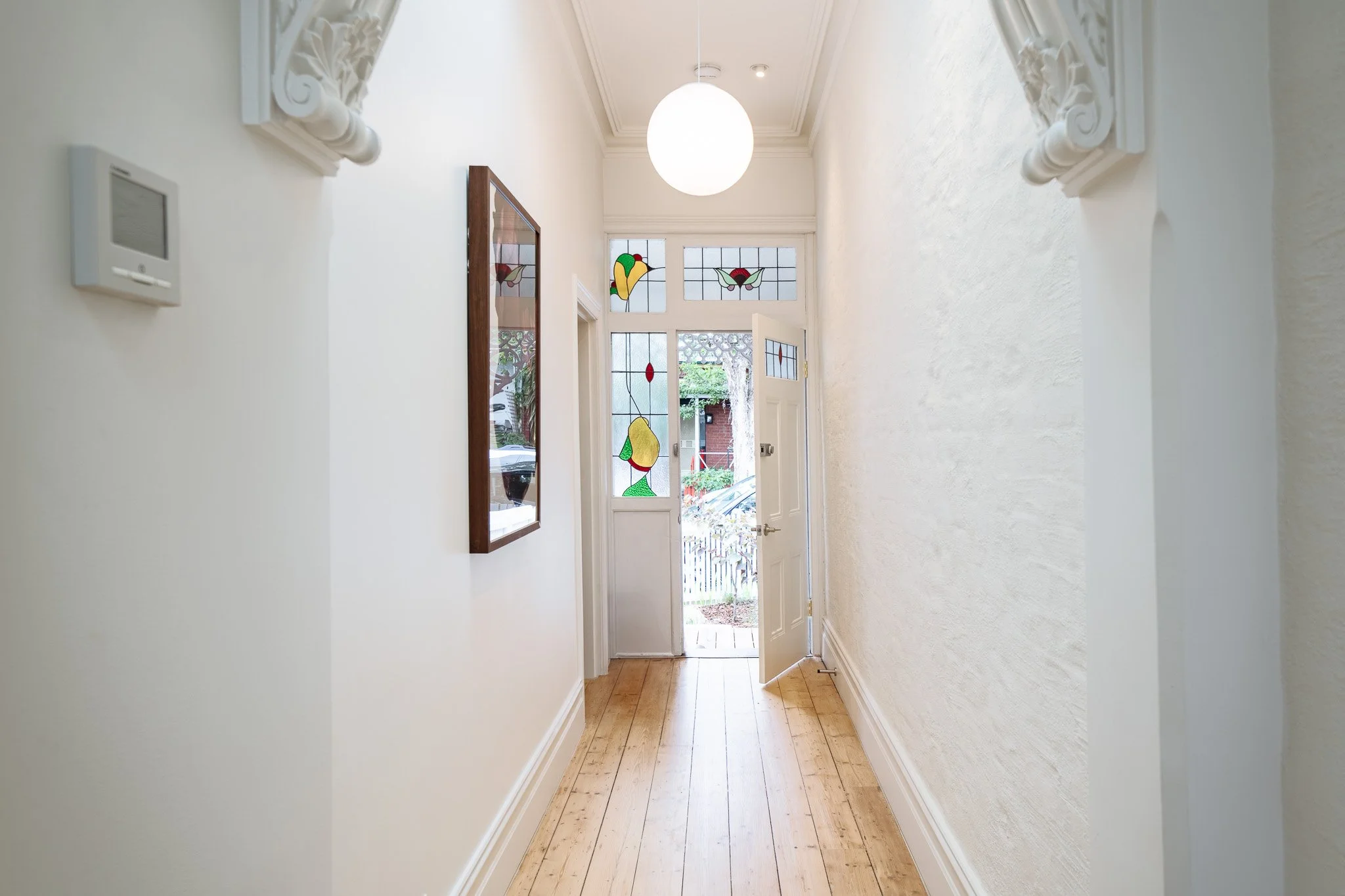Bright hallway with white walls, wooden floor, decorative molding, stained glass window above door, and a globe pendant light.