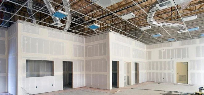 Interior of a building under construction with exposed ceiling framing and partially finished drywall on the walls.