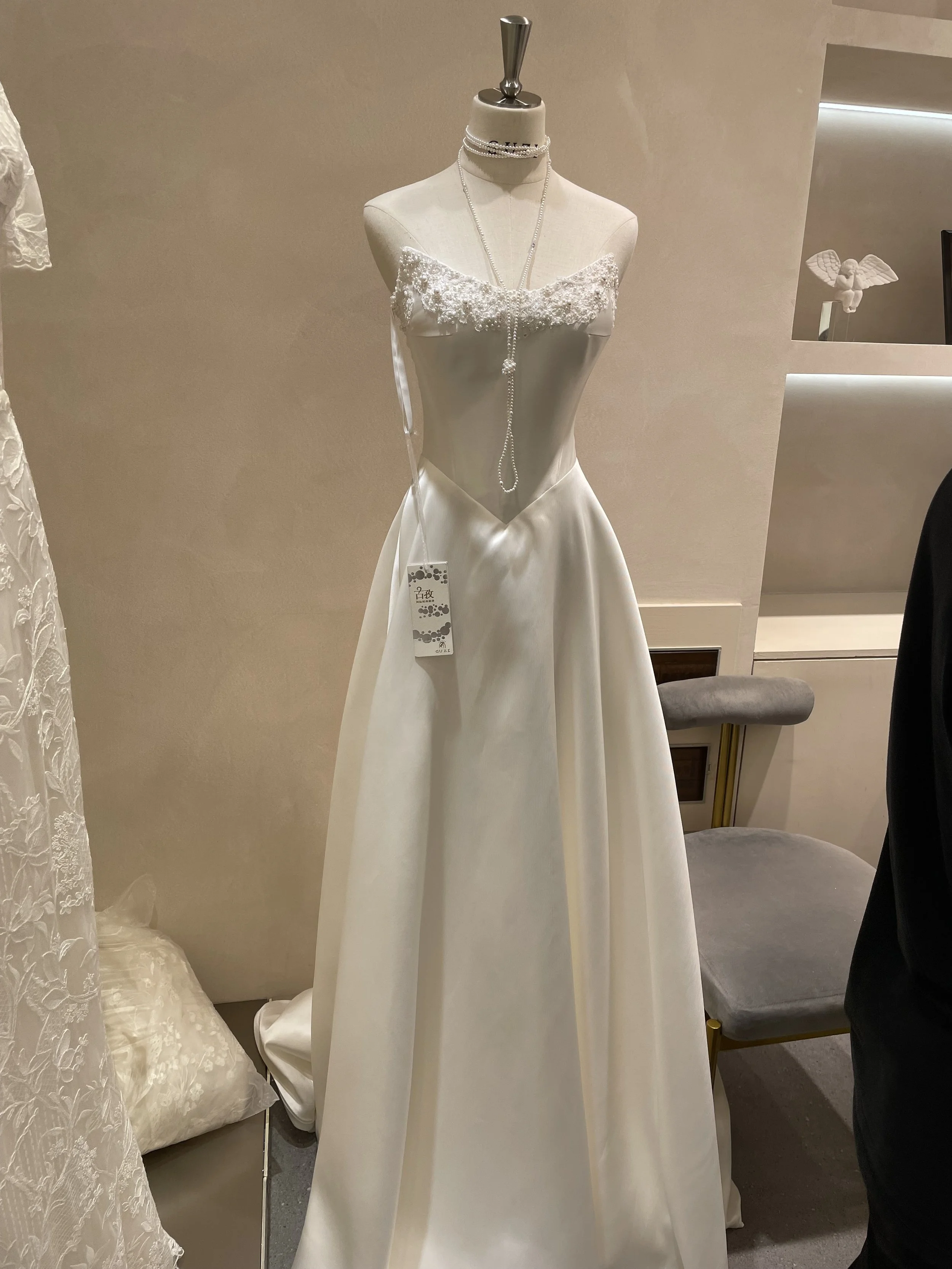 A white wedding dress on a mannequin, with lace and beaded details, displayed in a bridal shop.