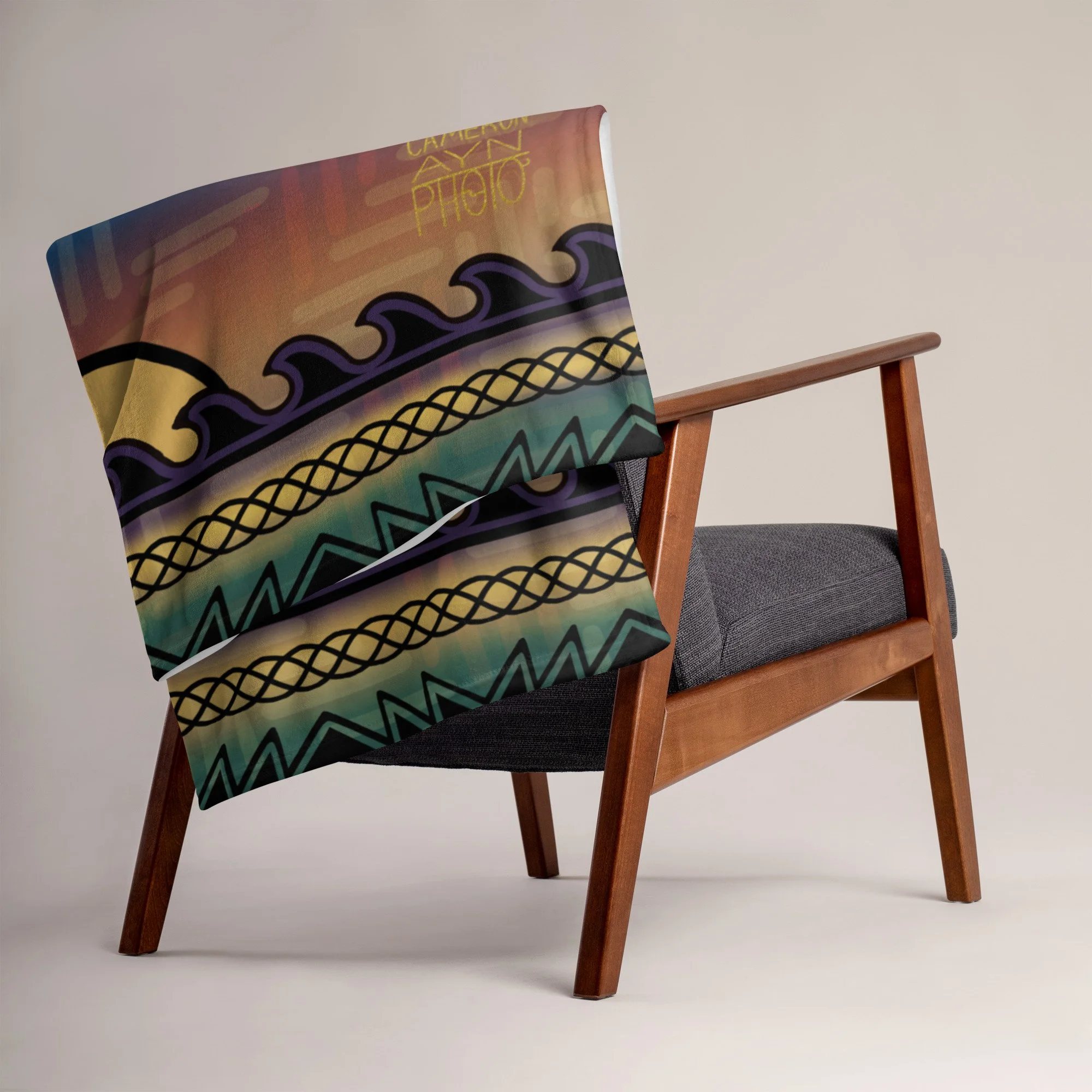 A chair with a colorful patterned blanket draped over its backrest. The fabric features a mix of geometric designs in black, yellow, purple, and teal colors highlighting authentic Cherokee patterns and designs. Native American owned business.