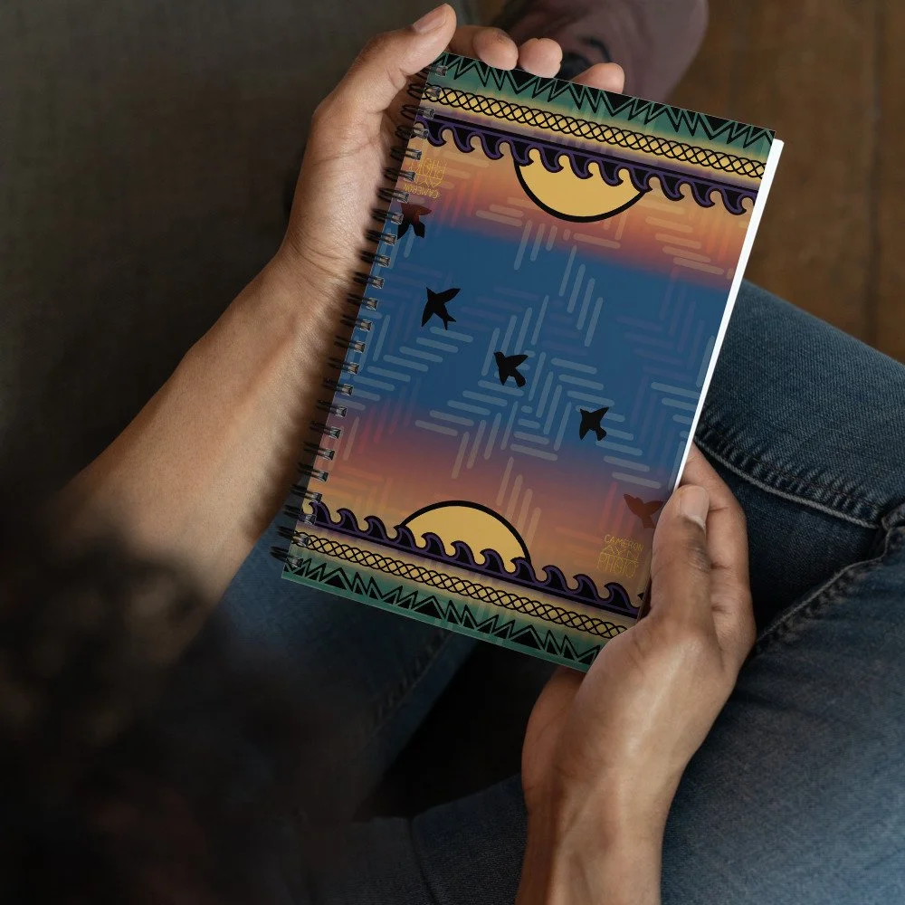 Person holding a spiral notebook with a colorful abstract sky and bird silhouettes on the cover featuring authentic Cherokee designs.