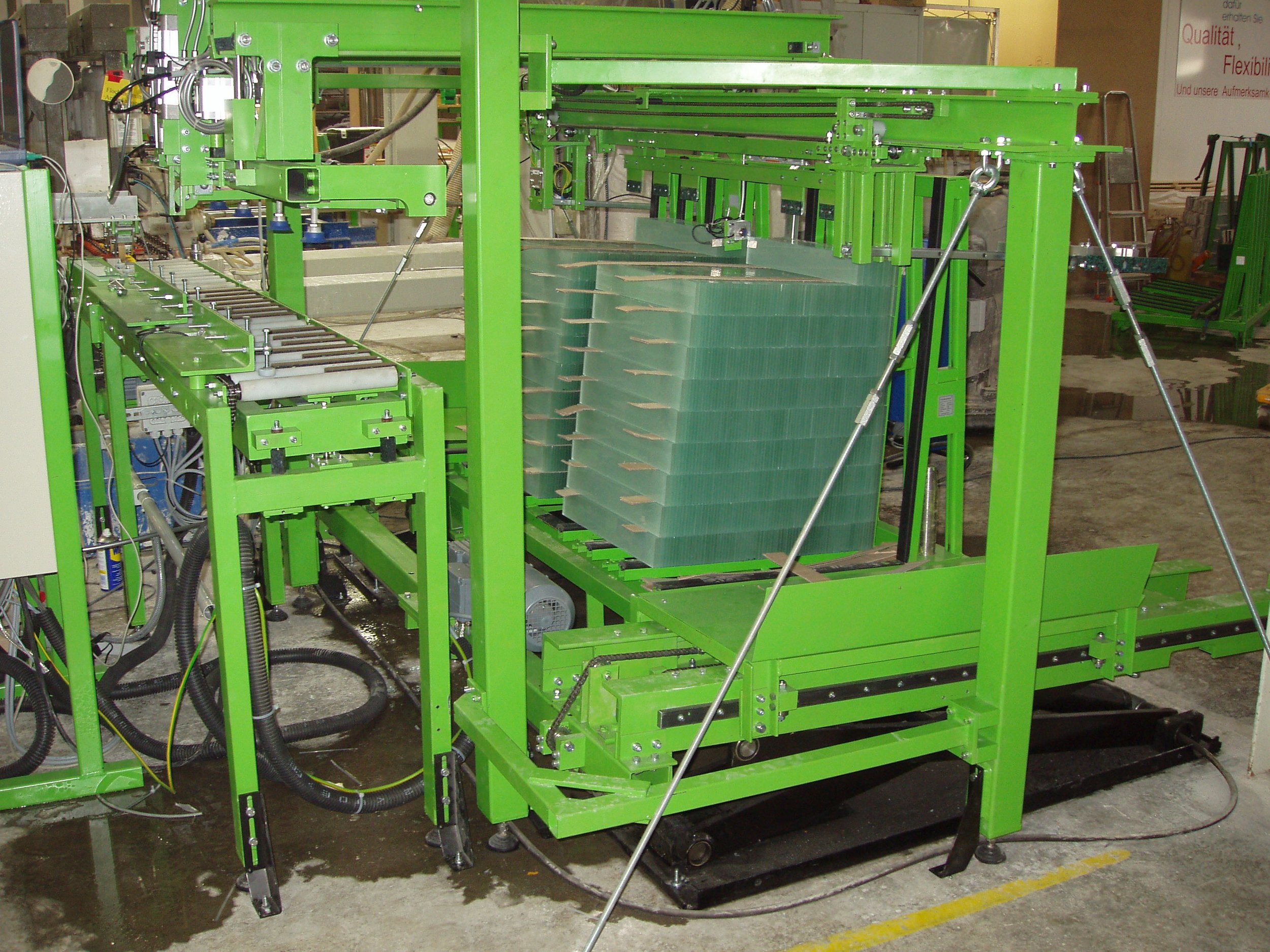Grüne industriell gefertigte Maschine mit mehreren Ebenen und beweglichen Teilen, vermutlich für die automatische Montage oder Verpackung.