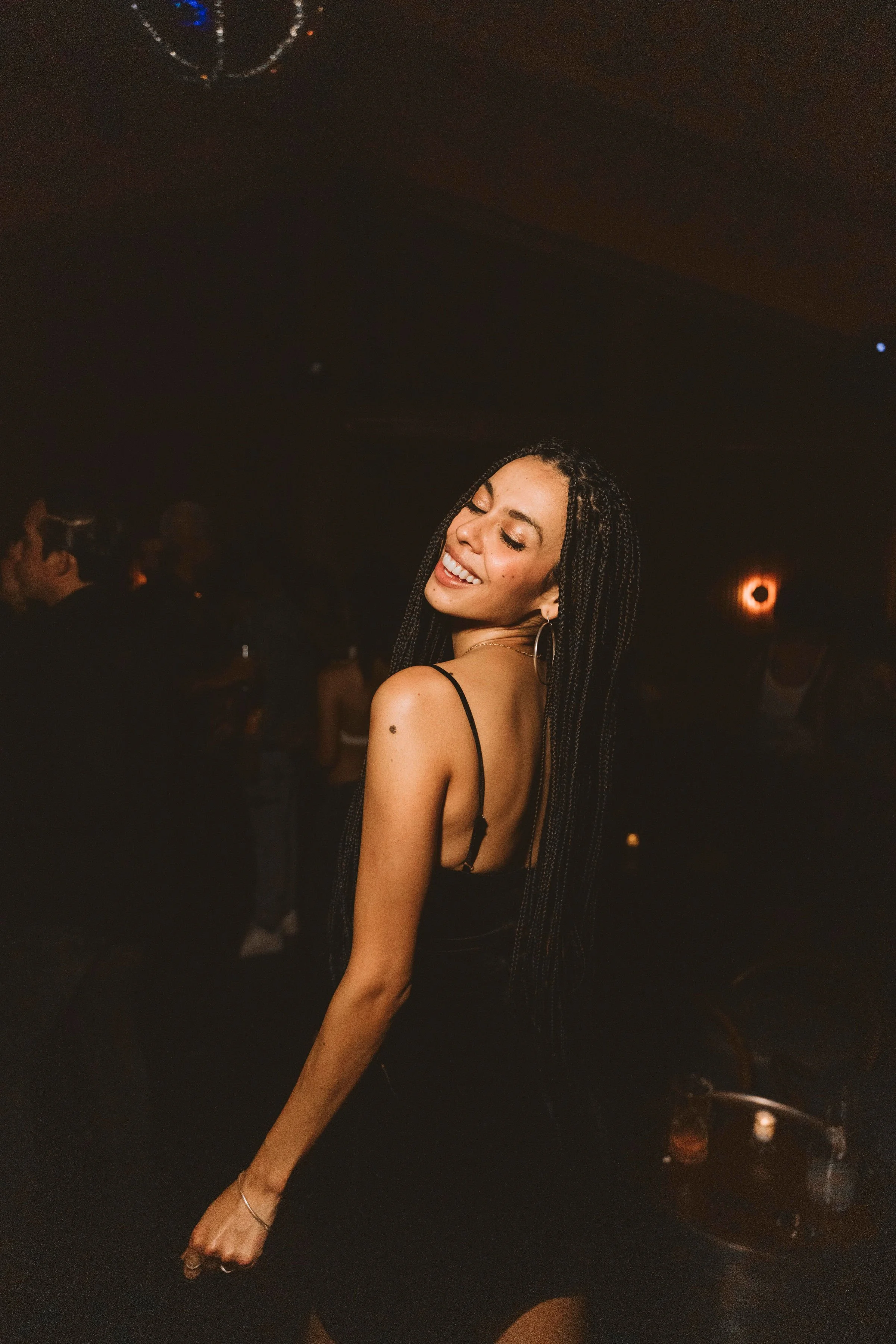 A woman with long braided hair smiling with her eyes closed in a dimly lit nightclub at a Casa de Afro party by Dr. ADO in Mexico City.