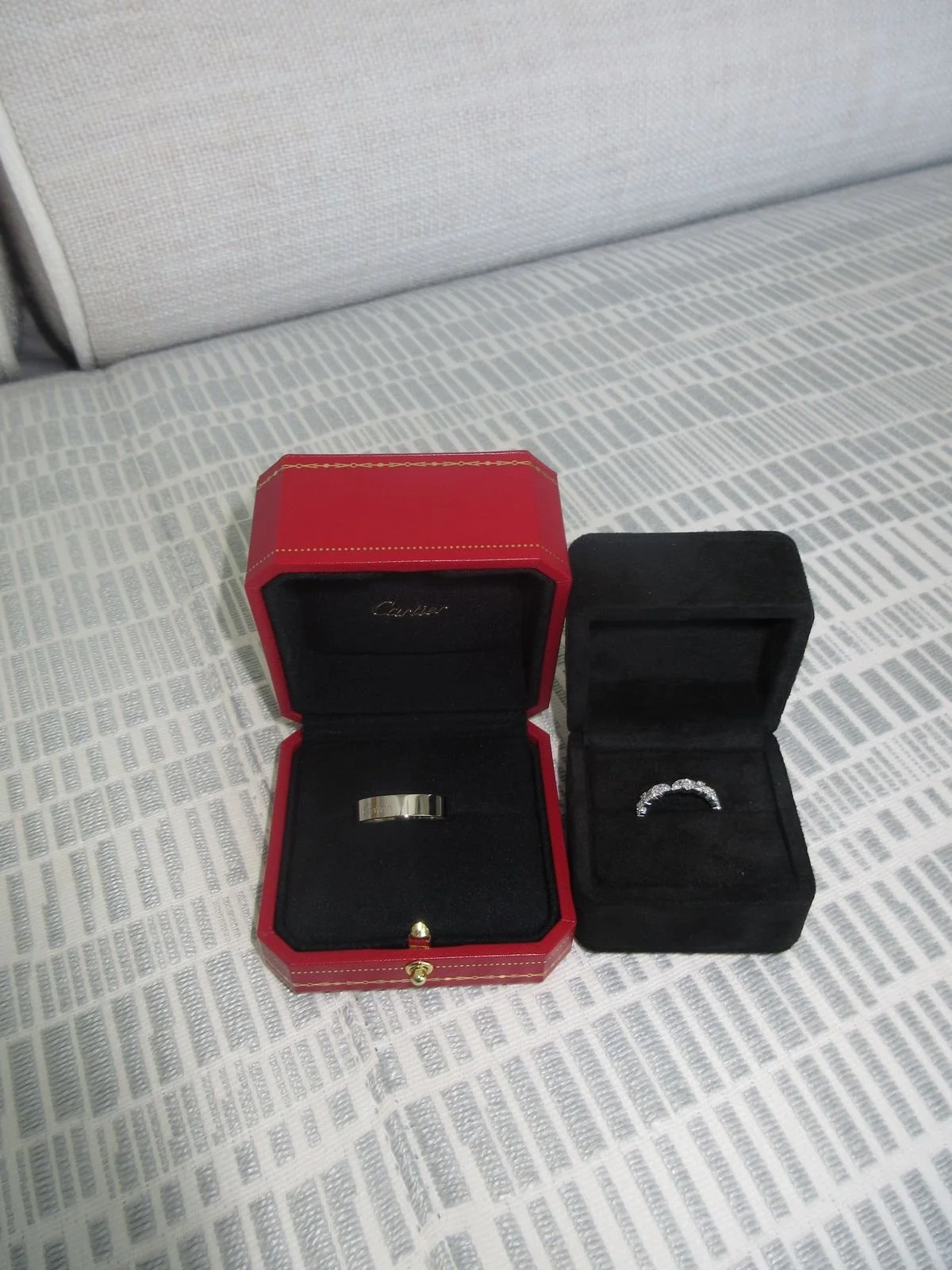 Two jewelry boxes, one red with a ring inside and one black with a diamond ring, placed on a patterned fabric surface.