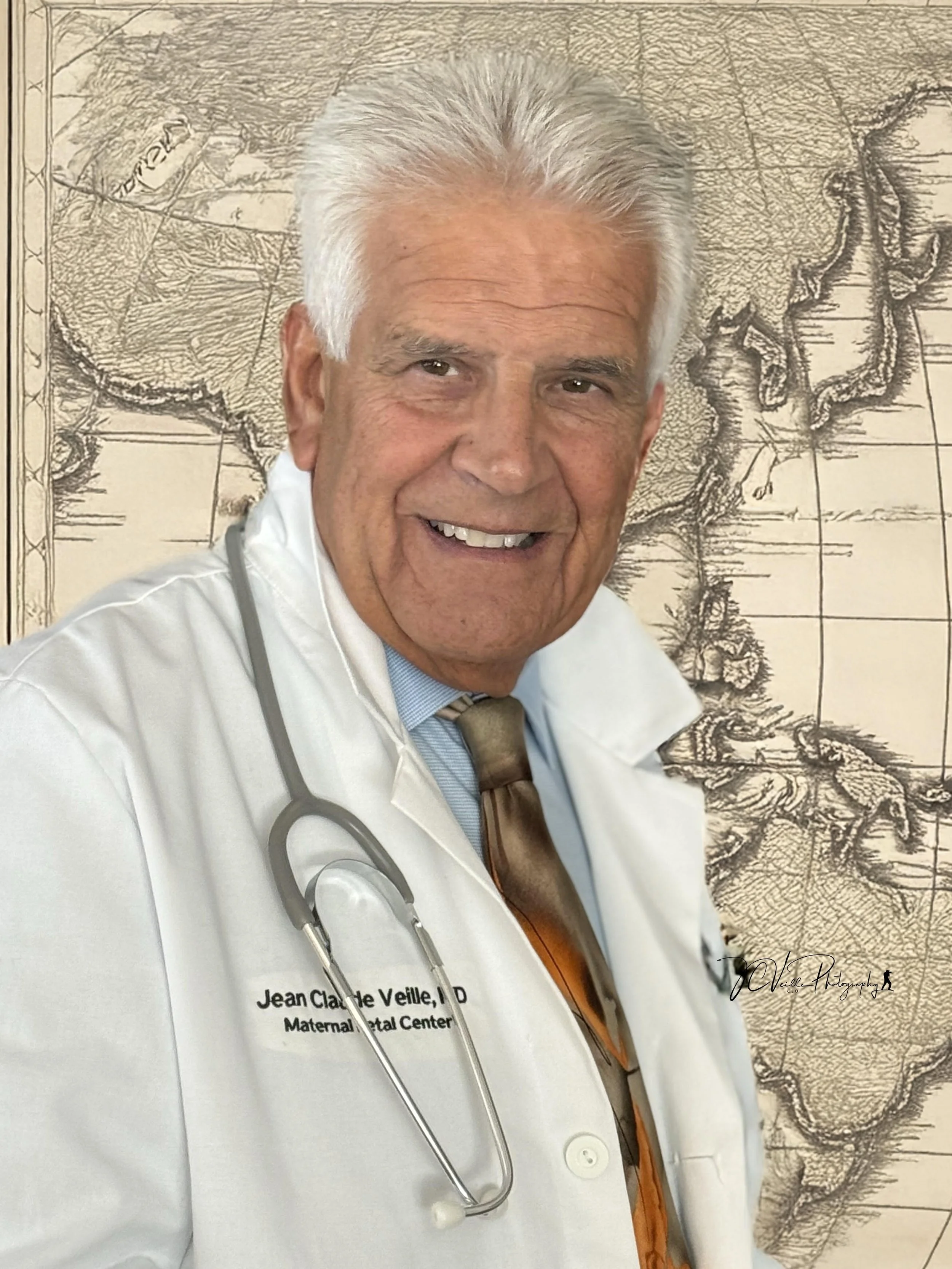 A smiling elderly male doctor with white hair, wearing a white lab coat with a stethoscope around his neck, standing in front of a vintage map.