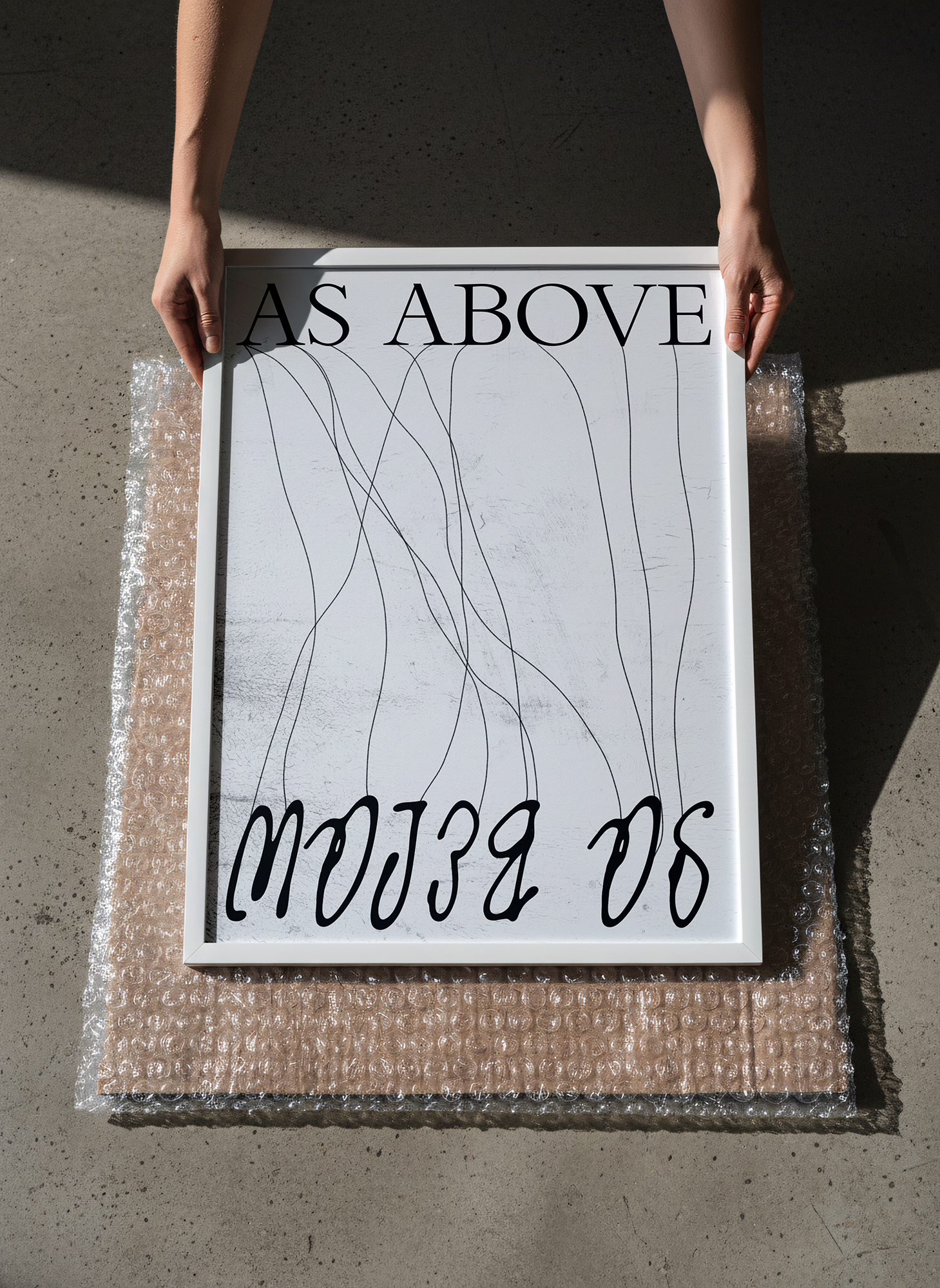 Close-up of a sign with the phrase 'AS ABOVE SO BELOW' held by two hands, with bubble wrap beneath the sign on a concrete surface.