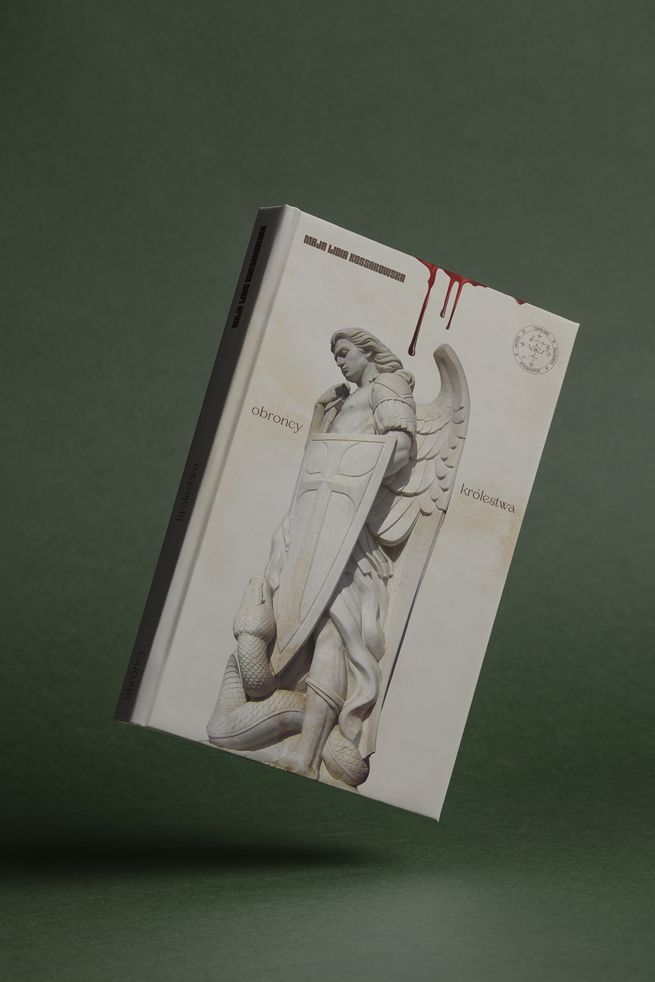A hardcover book with a cover illustration of a winged warrior angel holding a tshield and a serpent coiled at his feet, titled 'obroncy królestwa' by Maja Ludia Kossakowska, floating against a green background.