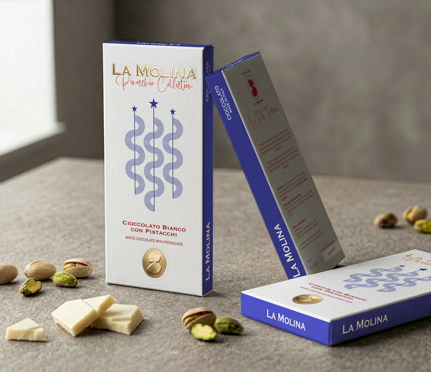 Three boxes of La Molina white chocolate with pistachios on a gray surface, with white chocolate pieces and pistachios scattered around.