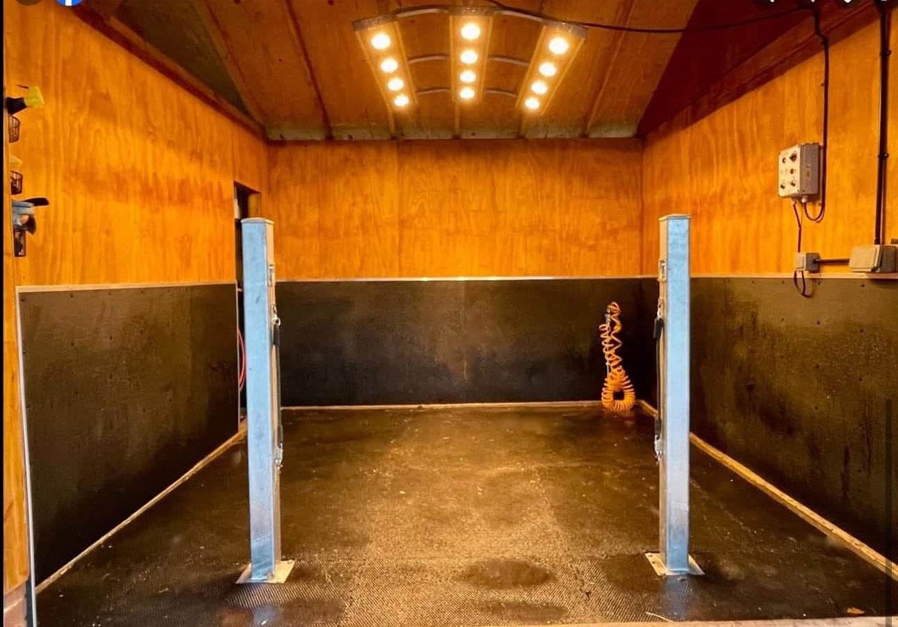 Wash bay with black rubber flooring, wooden walls, and overhead lights, featuring cross ties.