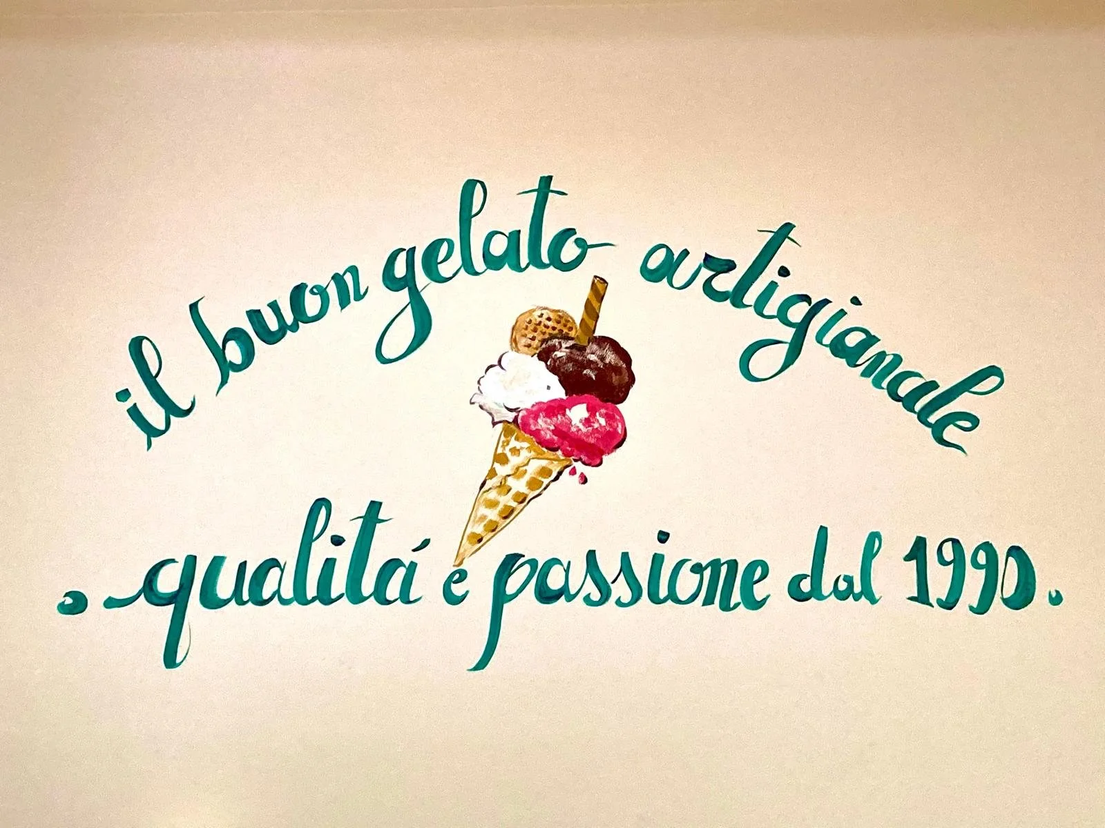 Decorazione con scritta in italiano e immagine di un cono gelato con vari gusti e una cialda, testo che dice 'il buon gelato artigianale qualità e passione dal 1990'.