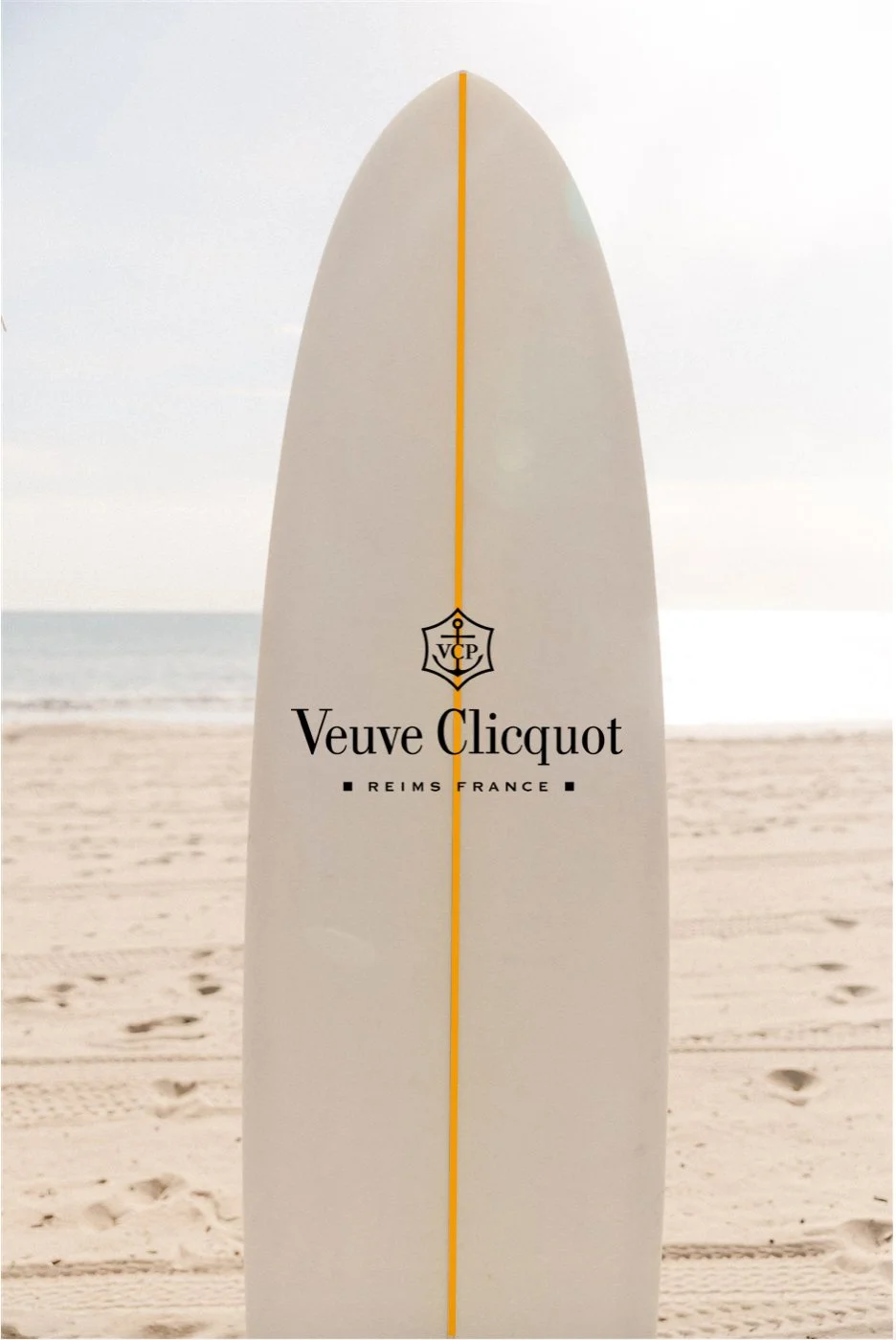 Surfboard with yellow stripe and company logo on the sand at the ocean
