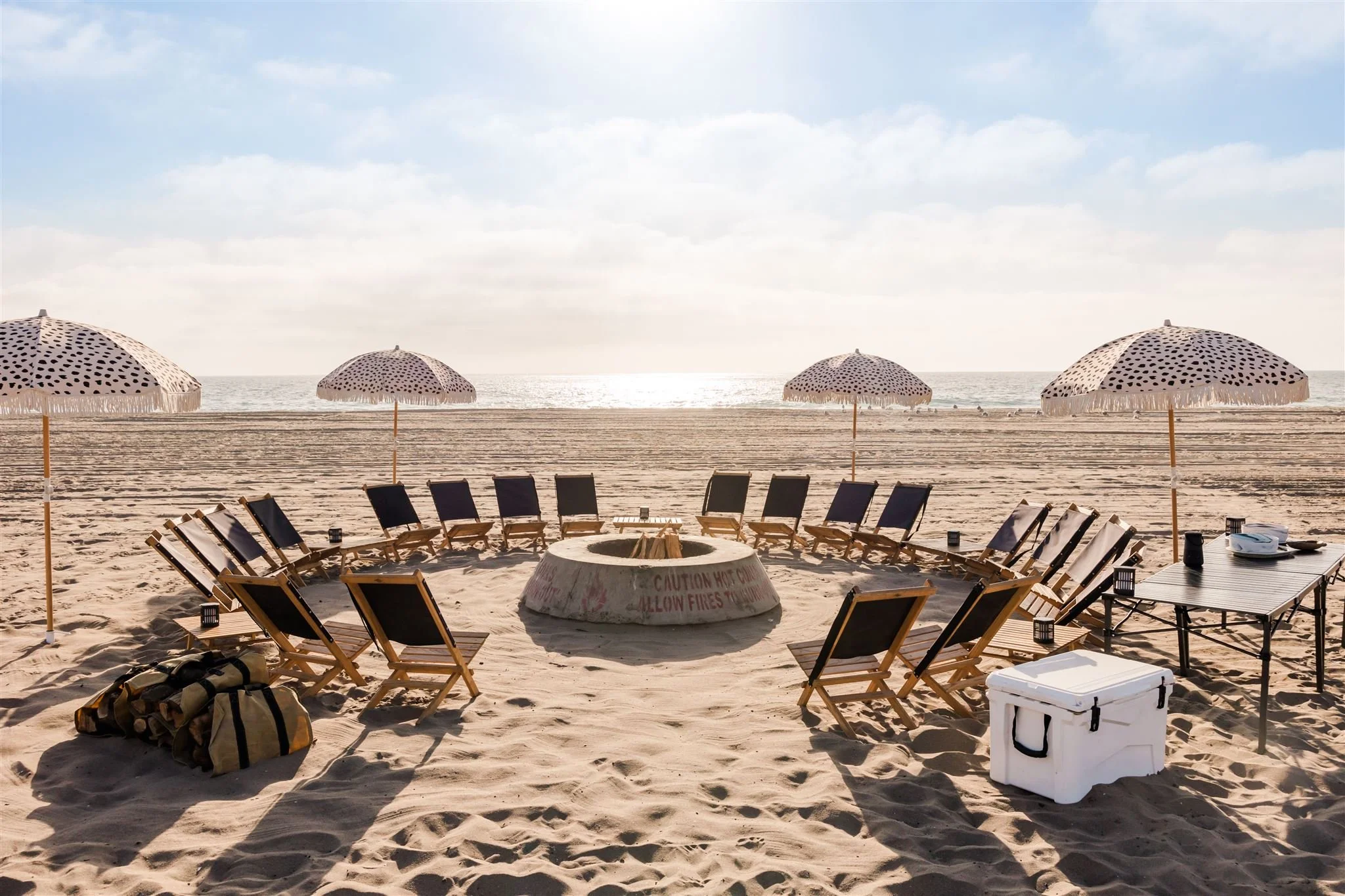 Beach bonfire with chairs around the fire pit with fire wood slat chairs and umbrellas