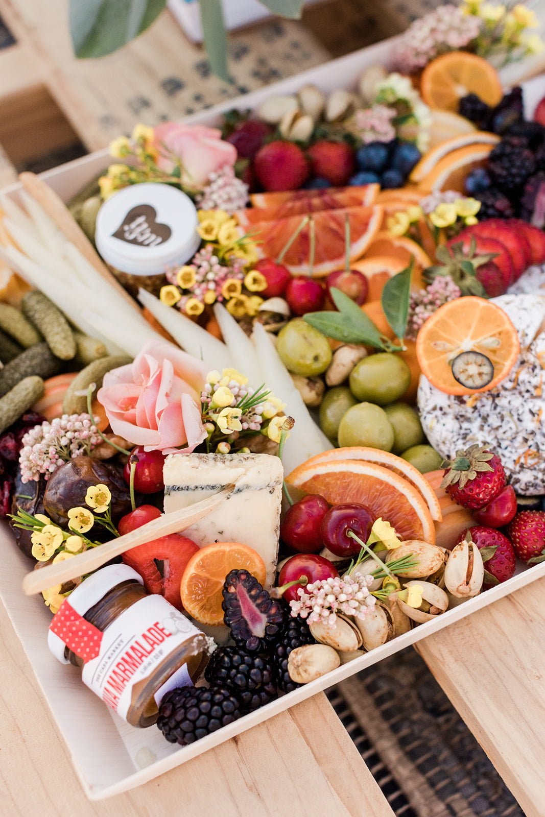 Charcuterie board with bright fruit cheese and florals at beach picnic
