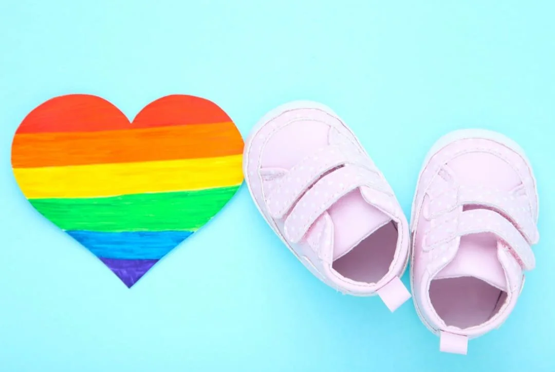 cuore arcobaleno e scarpe da bambino rosa su sfondo azzurro