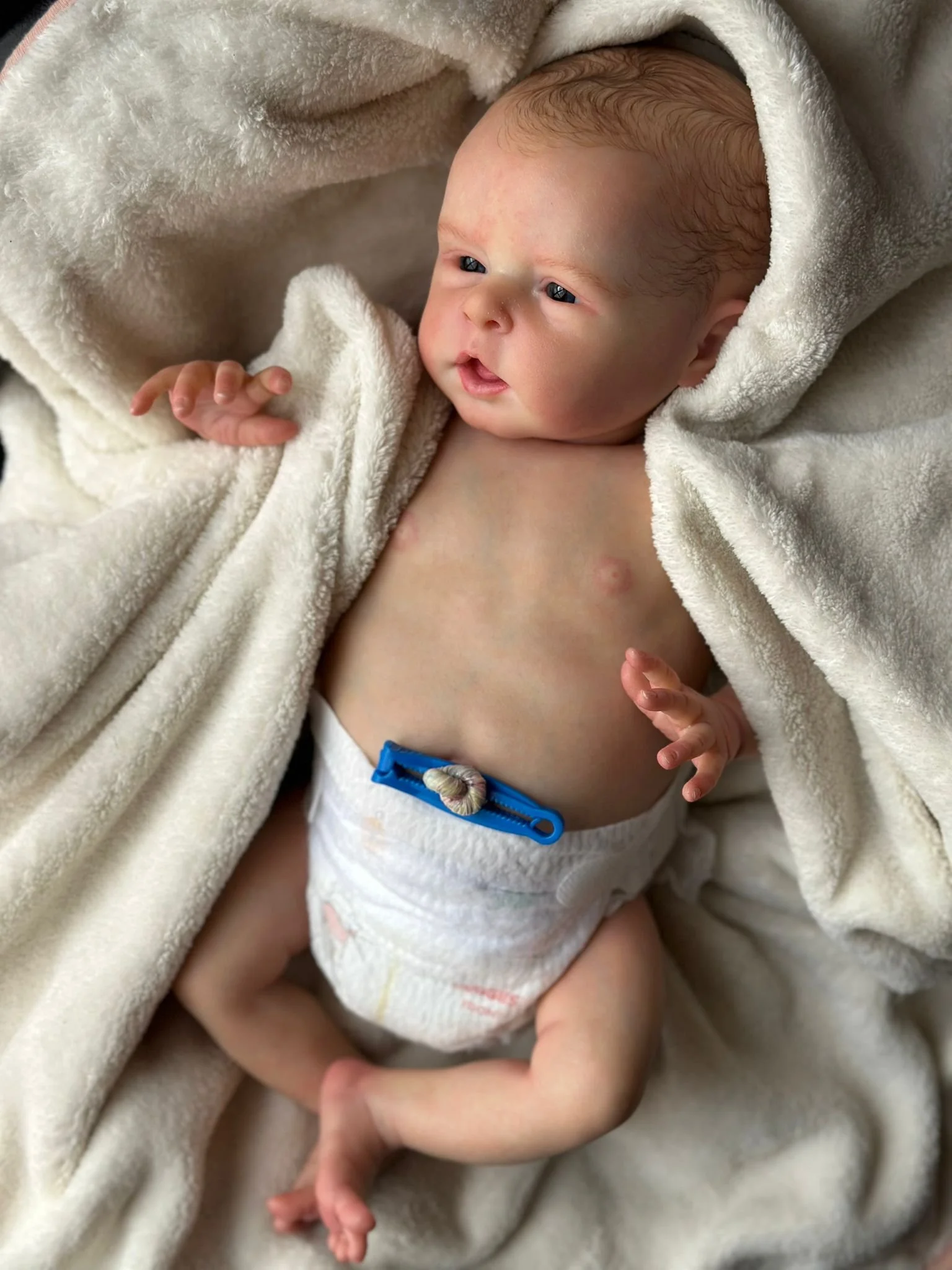 Neonatosdorme avvolto in una coperta bianca, con un pannolino e un piccolo peso blu, sdraiato su una superficie morbida di colore chiaro.