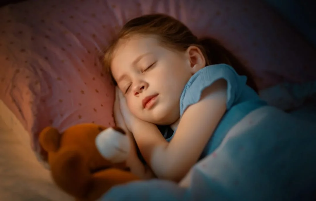 Una bambina che dorme serenamente nel letto, abbracciando un orsacchiotto di peluche.