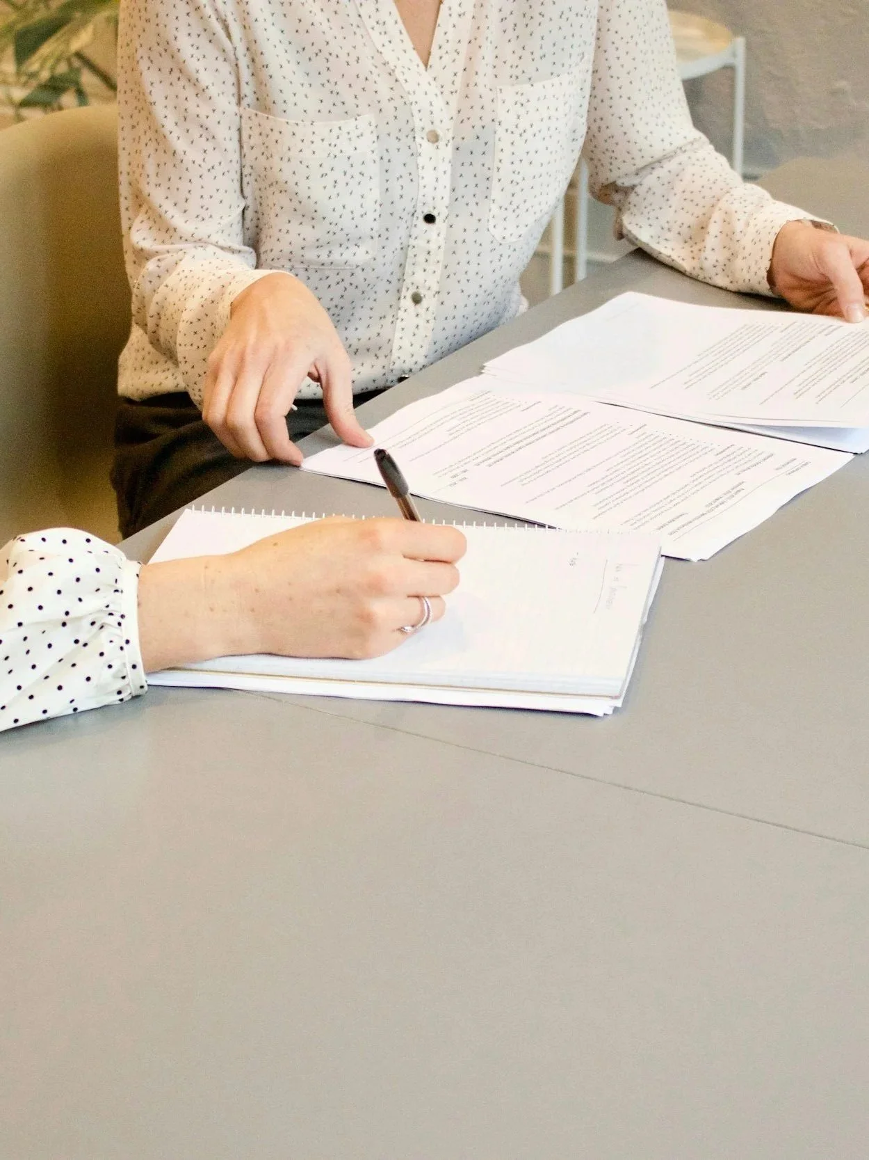 Kaksi henkilöä istuu pöydän ääressä ja tekee töitä, papereita ja kynä pöydällä.