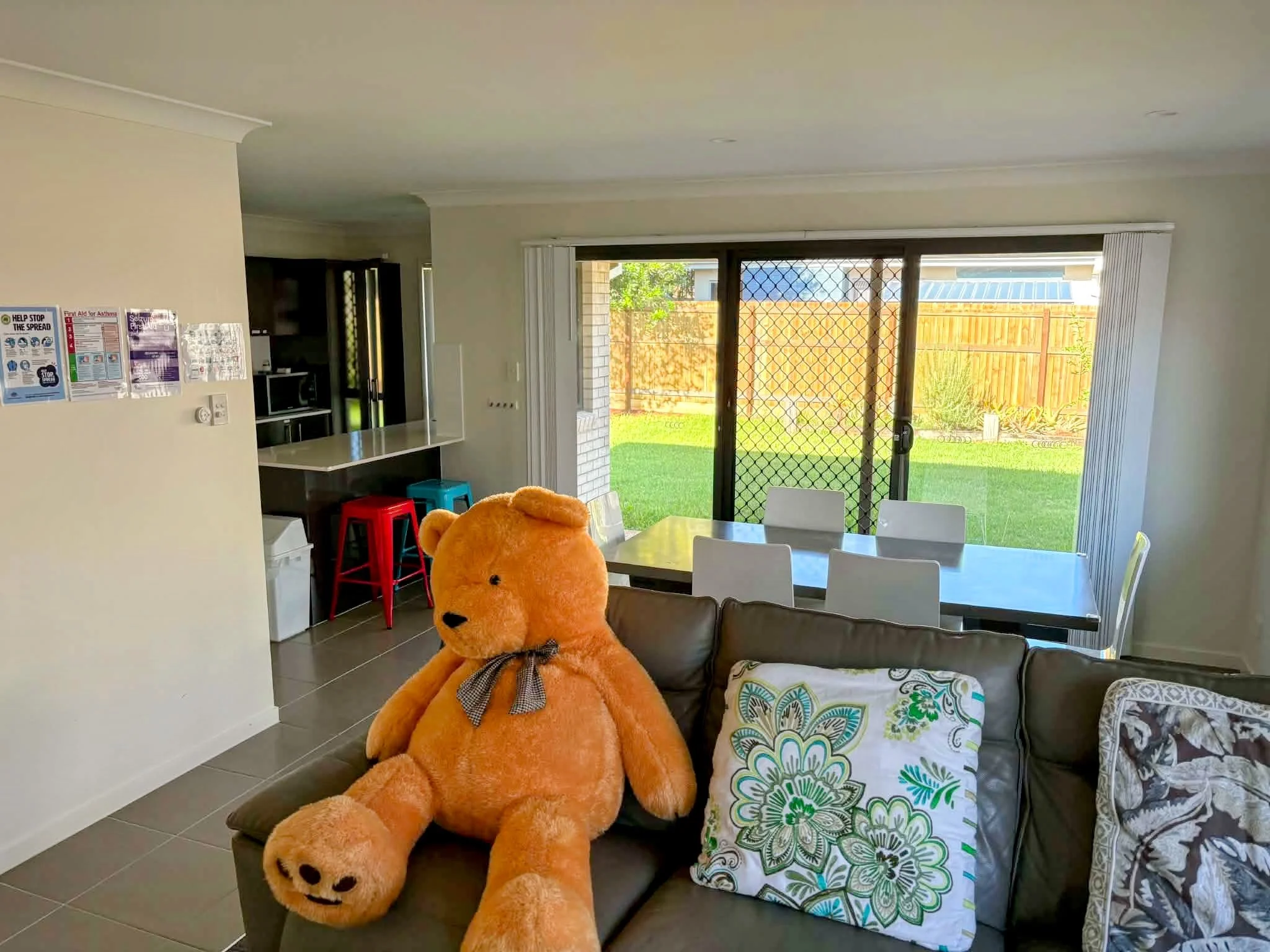 Living room with sliding glass door leading to backyard, decorated with cushions and a large orange teddy bear on the couch.
