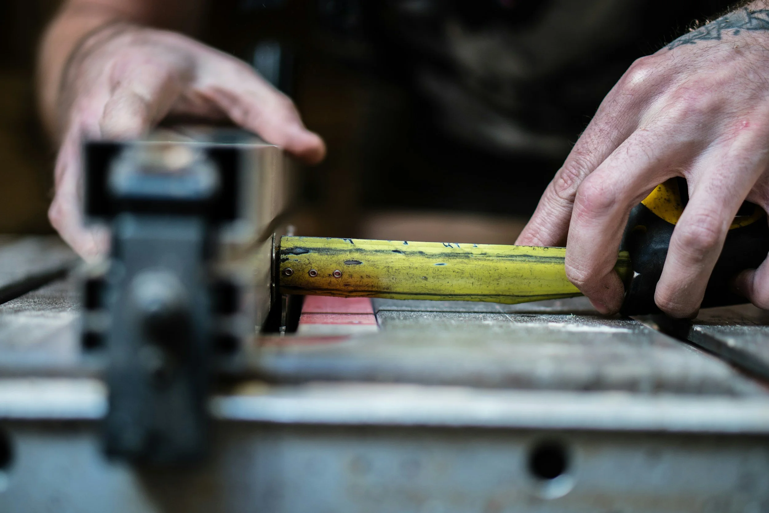 Close-up of hands using a yellow measuring tape on a metal surface, with a black measuring instrument nearby.