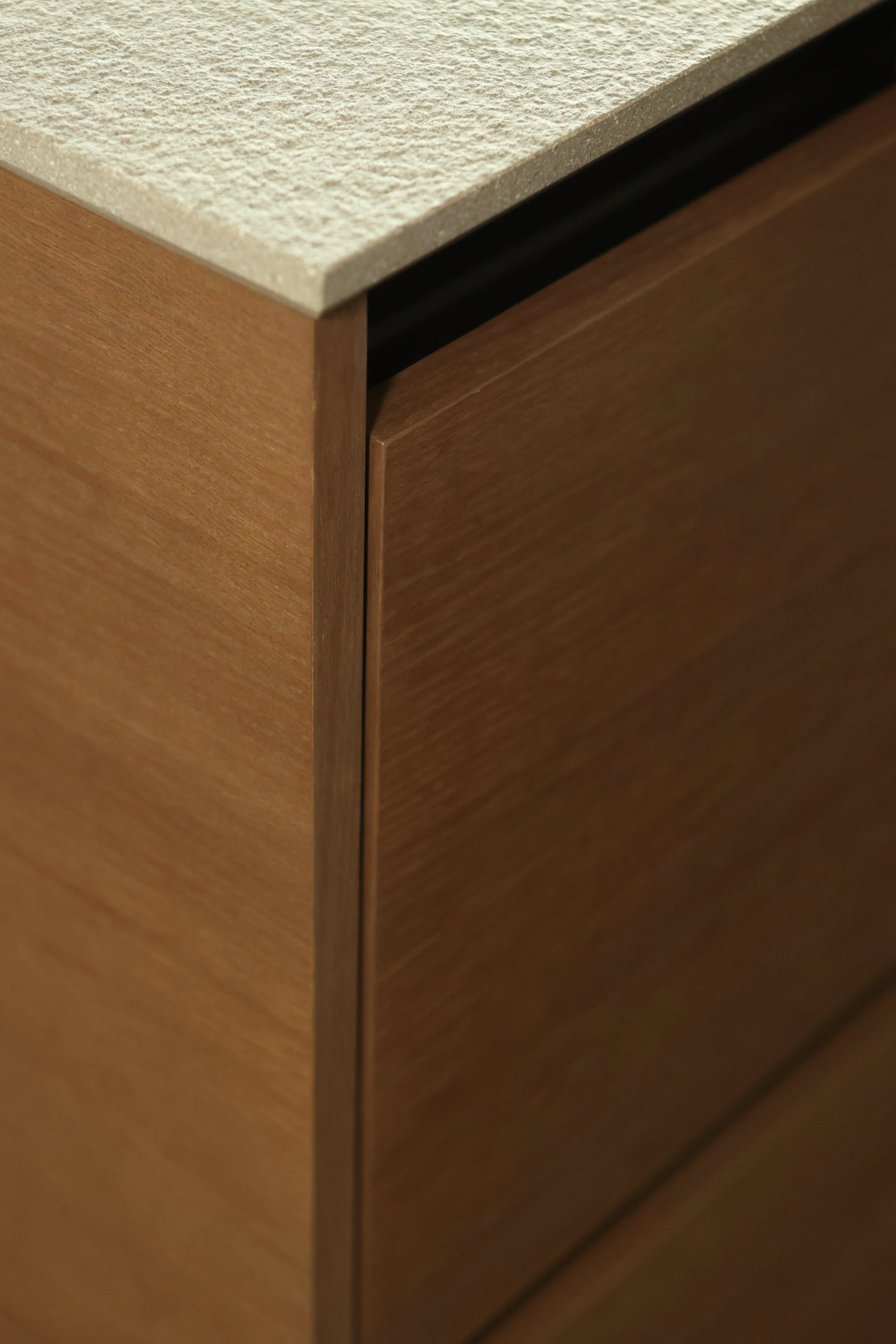 Close-up of a corner of a wooden cabinet with a beige stone or quartz countertop.