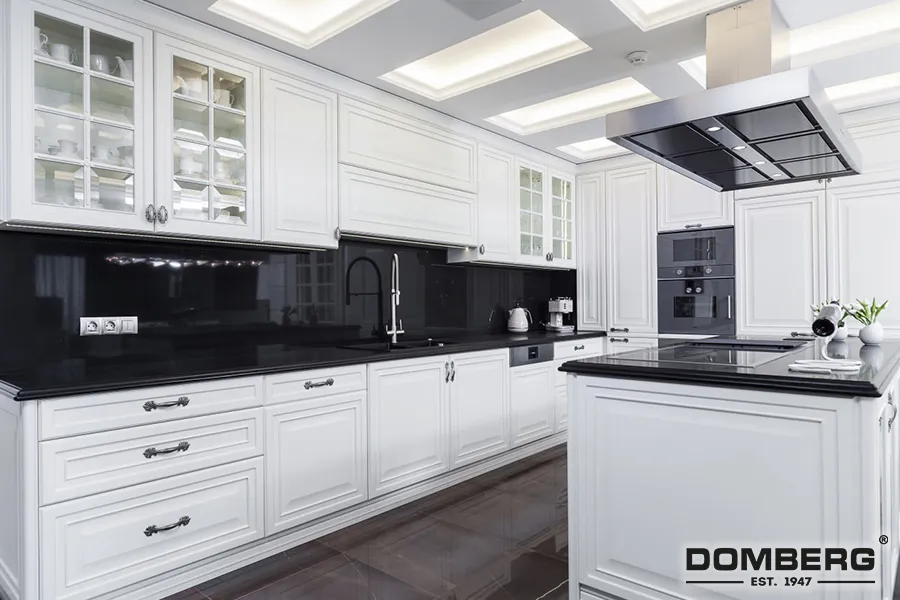 Modern white kitchen with black countertops, glass cabinet doors, built-in oven, and central island with a black stovetop.