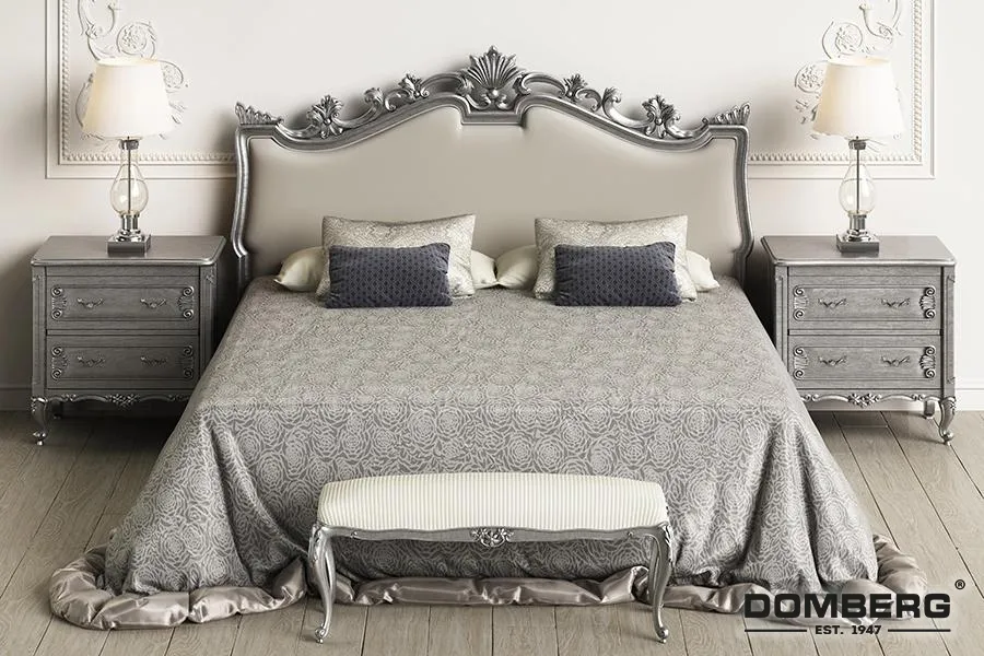 Elegant bedroom with a large upholstered bed, silver ornate headboard, two matching silver nightstands with lamps, and a matching silver bench at the foot of the bed.