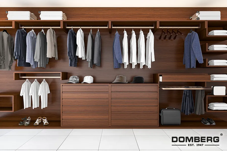 A modern closet with wooden shelves and hanging clothes, including shirts, jackets, and pants, along with shoes, hats, and storage boxes, featuring the DOMBERG logo in the bottom right corner.
