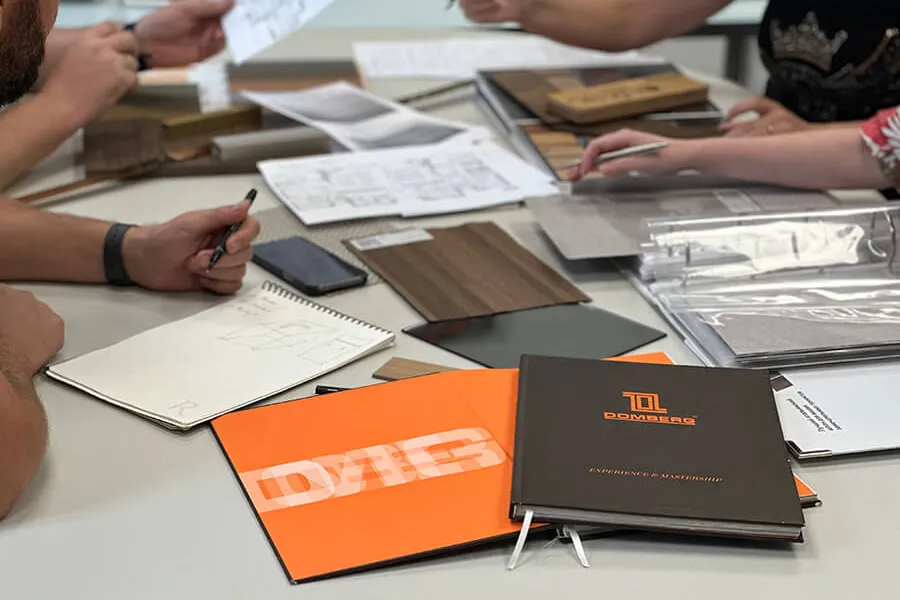 People working at a table with sample materials, notebooks, and fabric swatches for interior design or custom carpentry projects.