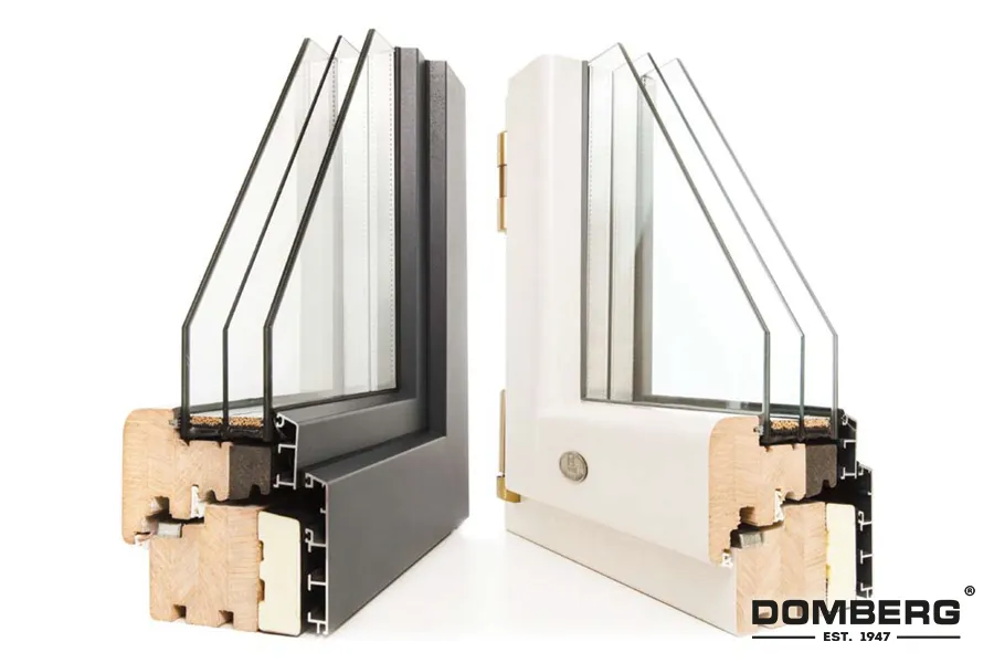 Cross-section of two window frames, one black and one white, displaying how the glass panes are installed within the frames with visible window hardware, and showing the wooden core of the frames for insulation. The Dombeg logo is in the bottom right corner.
