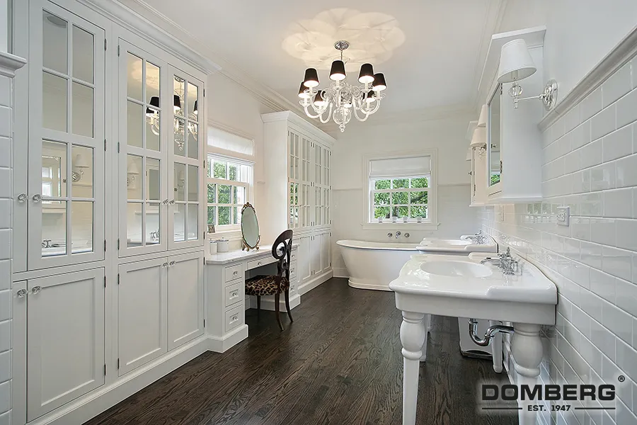 Bright white bathroom with two sinks, a freestanding bathtub, built-in cabinets with glass doors, and a chandelier.