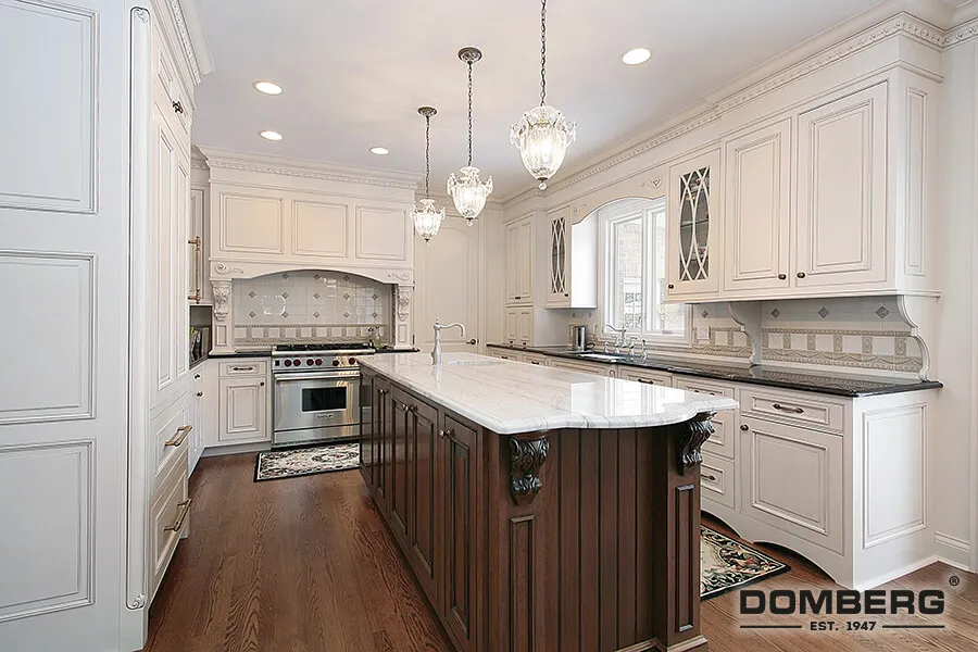White kitchen with a central dark wood island, white cabinetry with glass-paneled doors, stainless steel stove, granite countertops, and decorative hanging pendant lights.