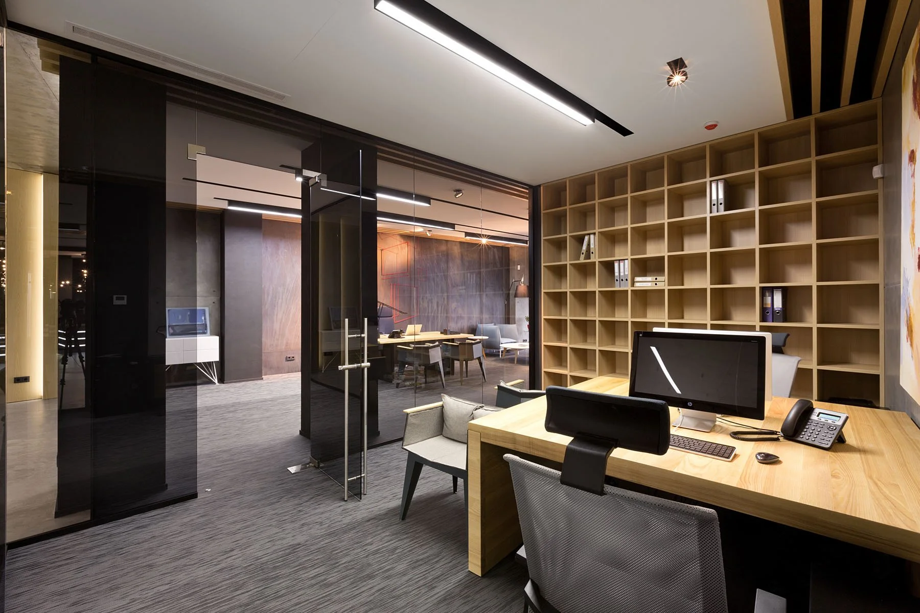 Modern office space with wooden desk, computer, office chairs, and a large wooden bookshelf in the background.