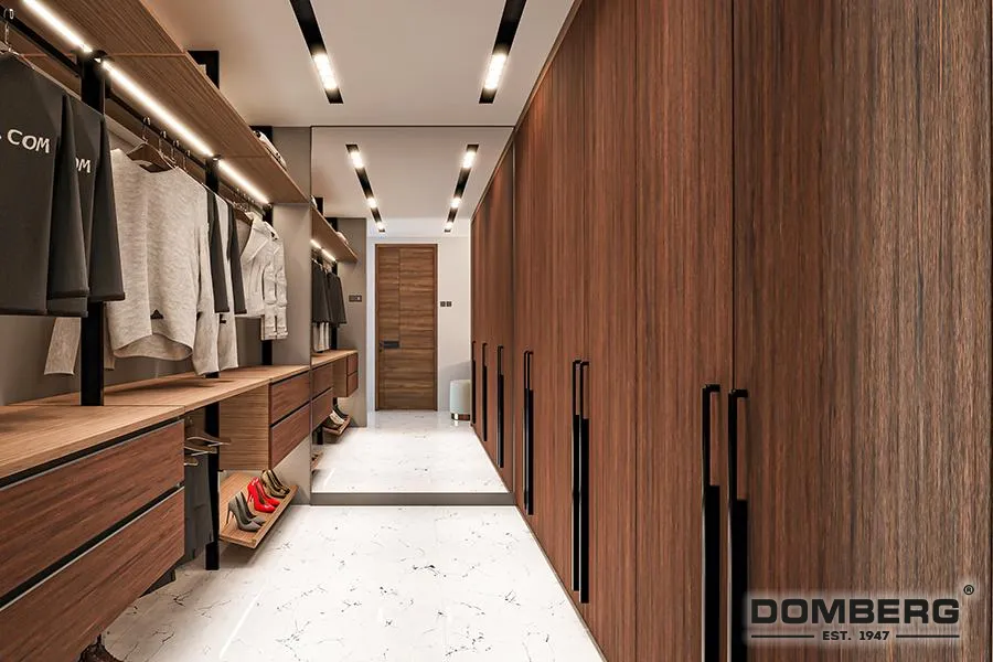 Modern walk-in closet with wooden storage cabinets on right and hanging clothes on the left, illuminated ceiling lights, white marble floor, and wooden door at the end.