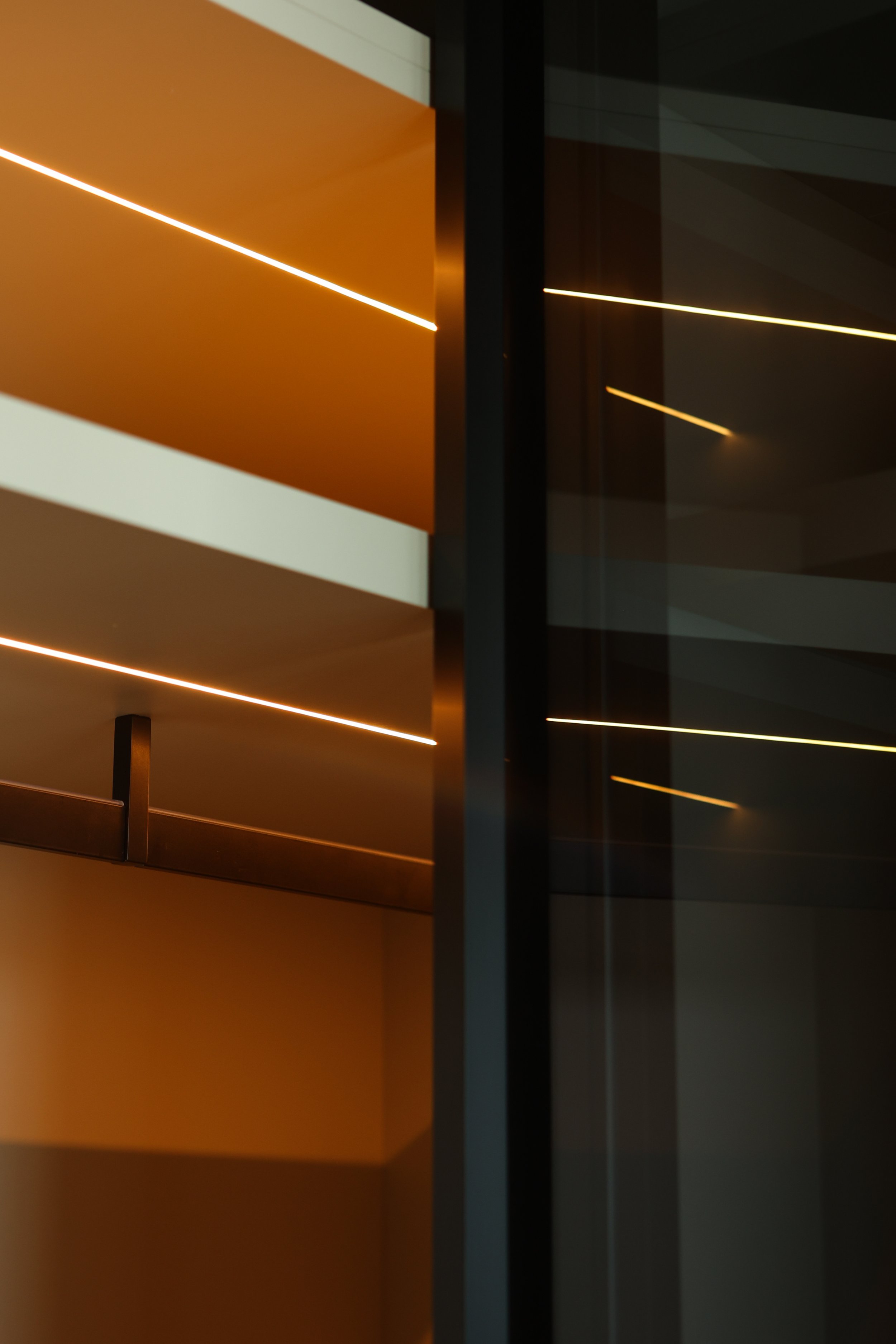 Close-up of an interior with modern ceiling lights, orange and dark-colored walls, and reflective glass surfaces.