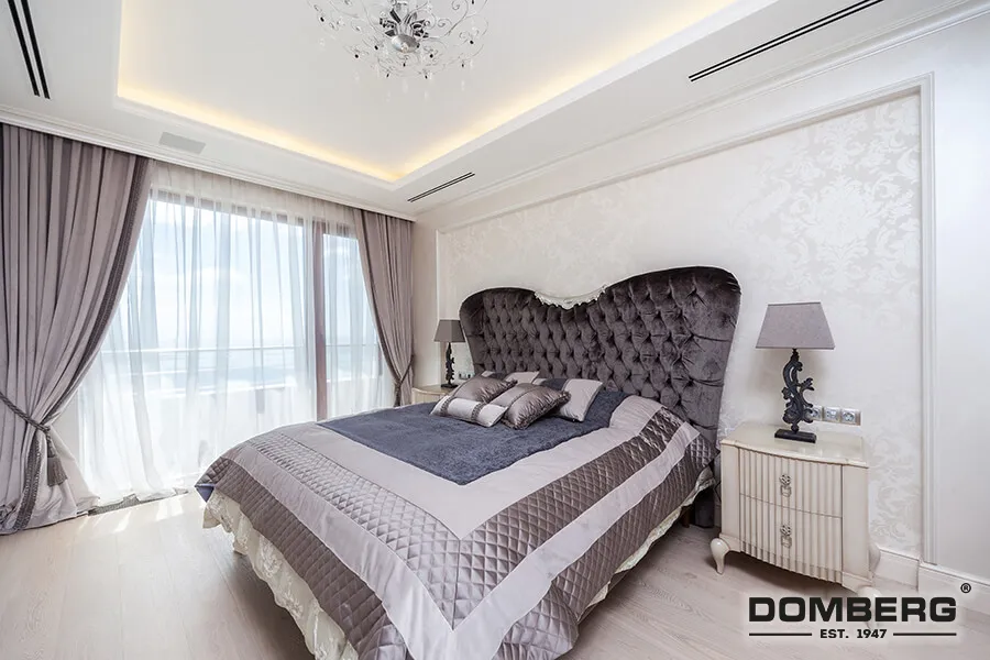 Elegant bedroom with a large tufted headboard, draped curtains, and a chandelier.