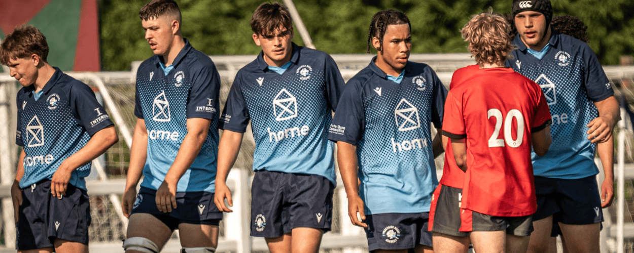 Youth soccer players on field, some in blue jerseys and one in red, during a game.