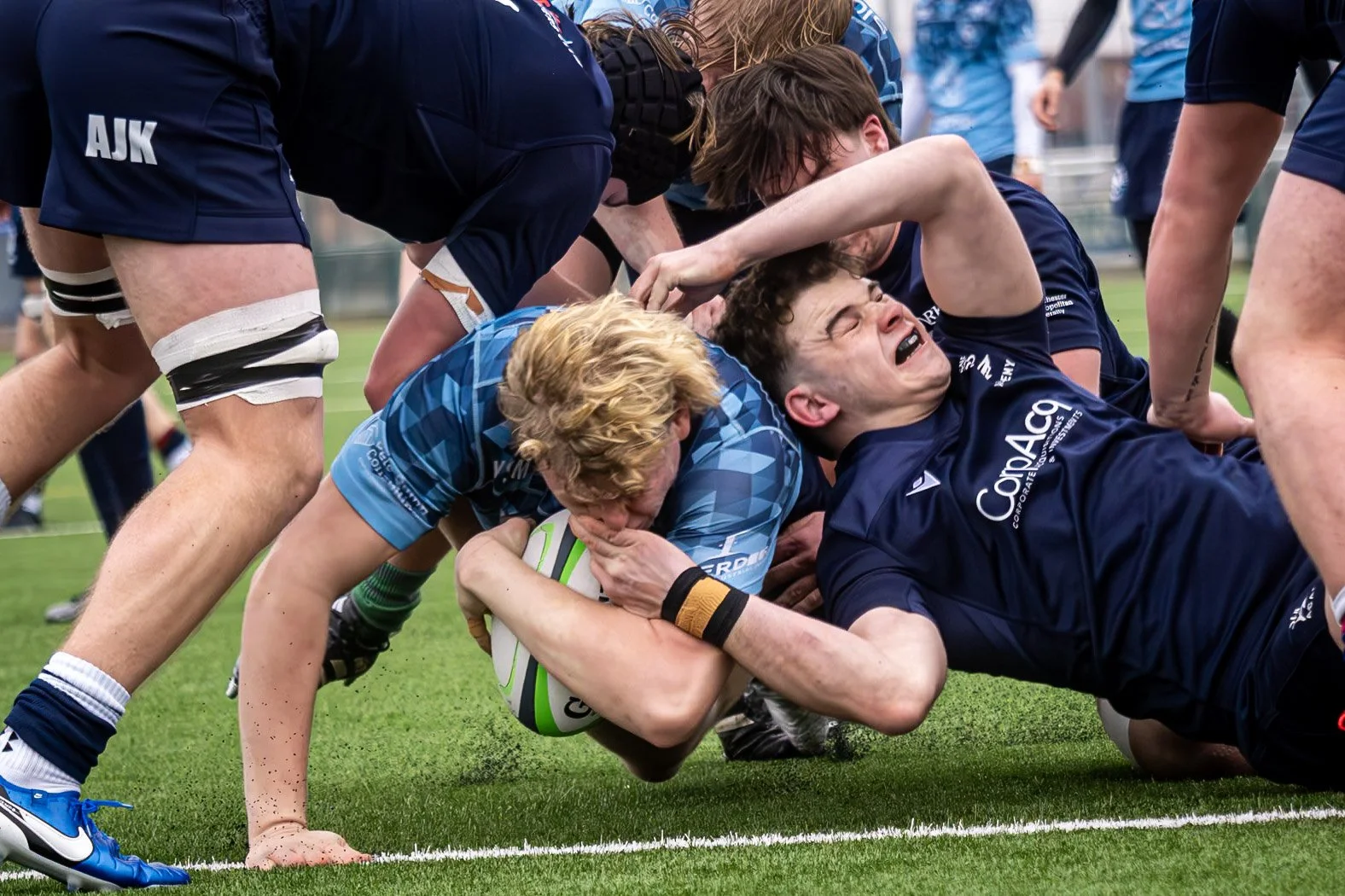 Rugby players in a fierce struggle on the field, with one player holding the ball while the others attempt to pull him down.