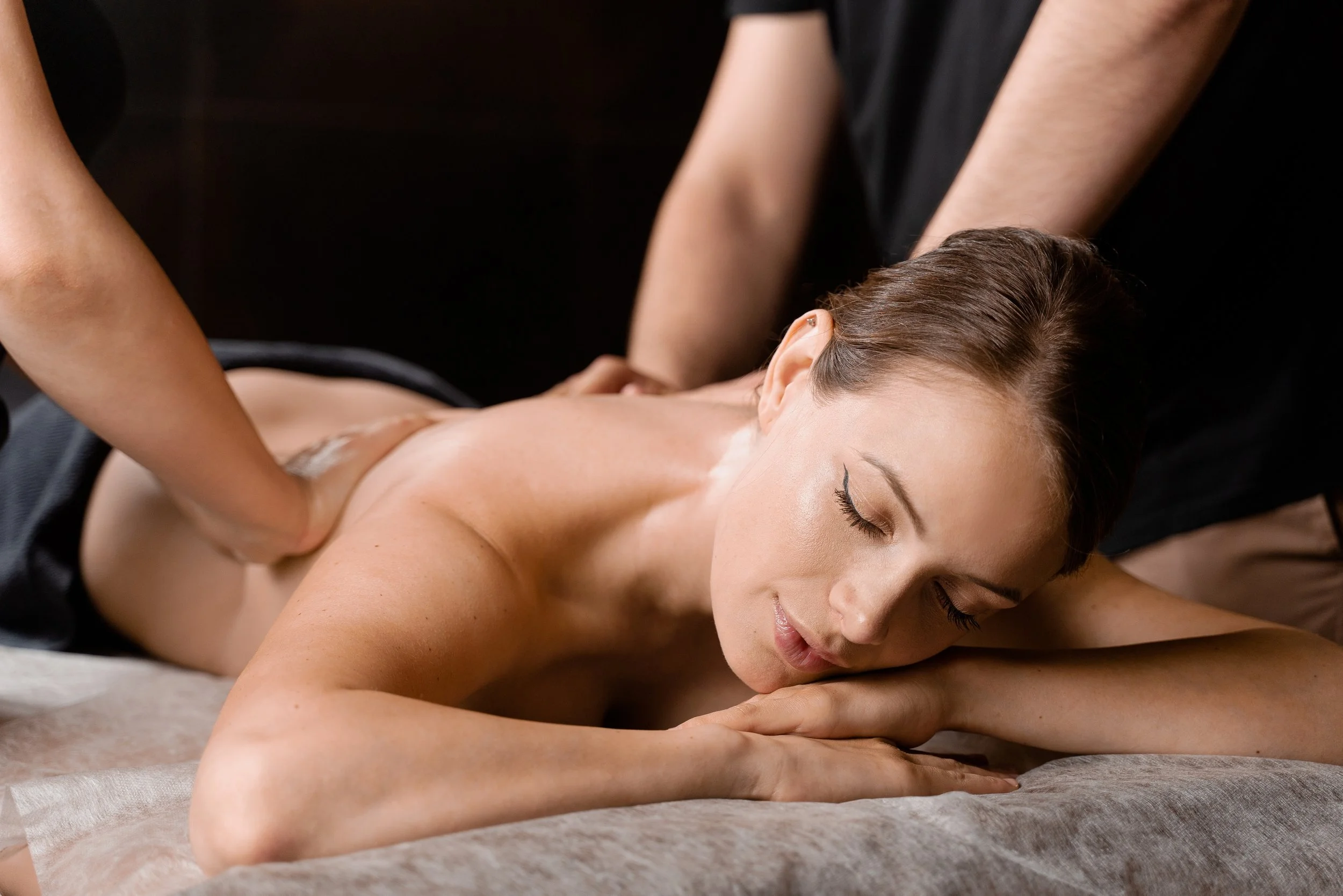 A woman receiving a massage while lying on a massage table with her eyes closed.