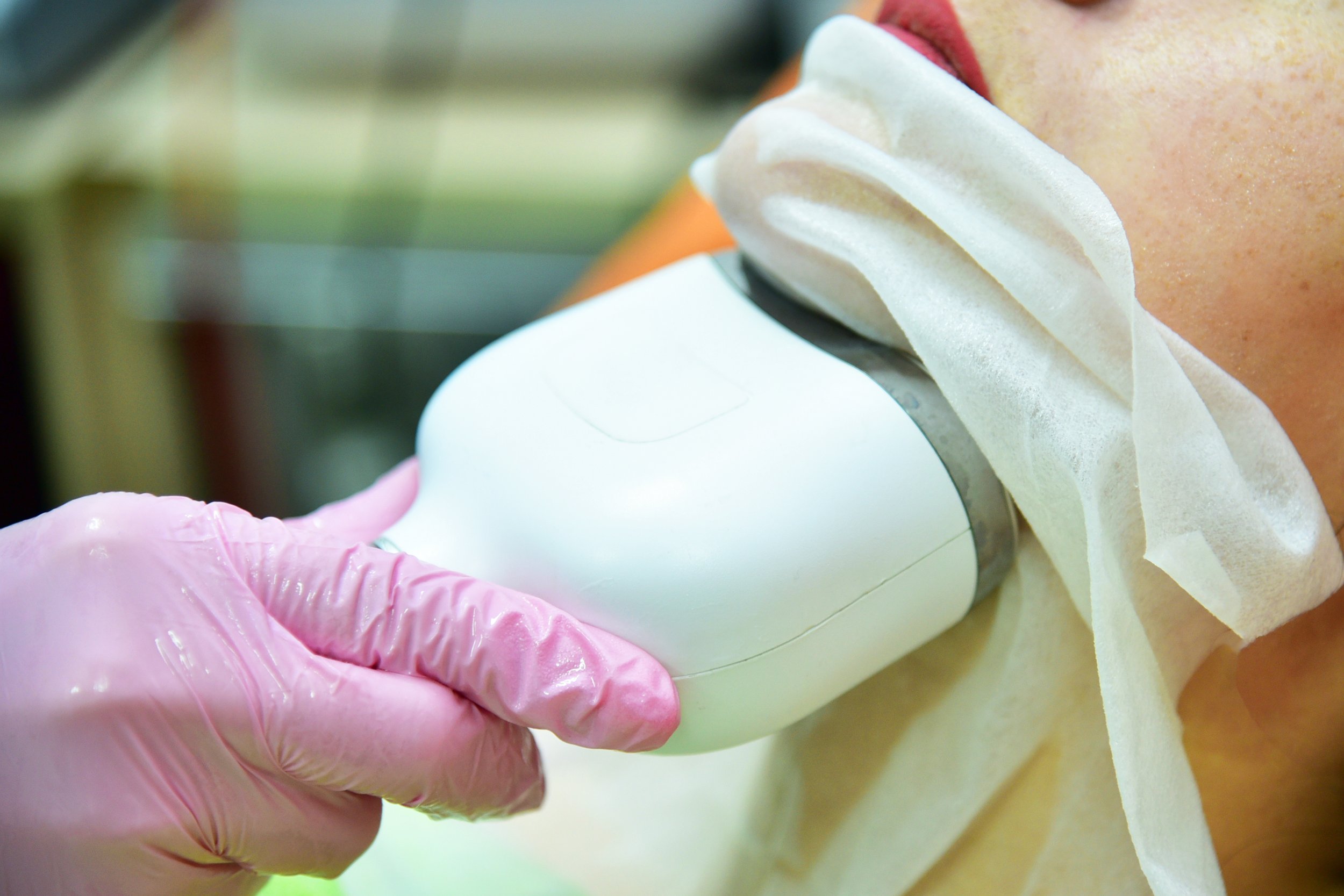 Medical professional in pink gloves using a handheld ultrasound device on a patient with a protective sheet covering their body.